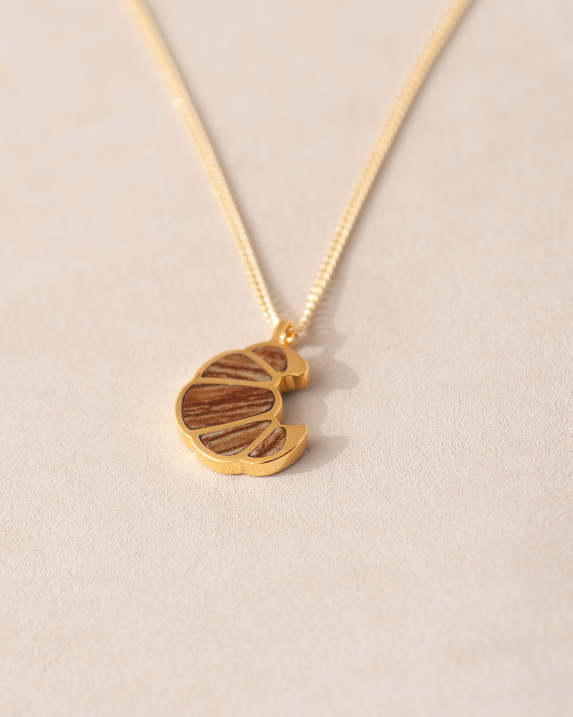 a gold charm shaped like a croissant, inlaid with jasper, dangling from a gold chain