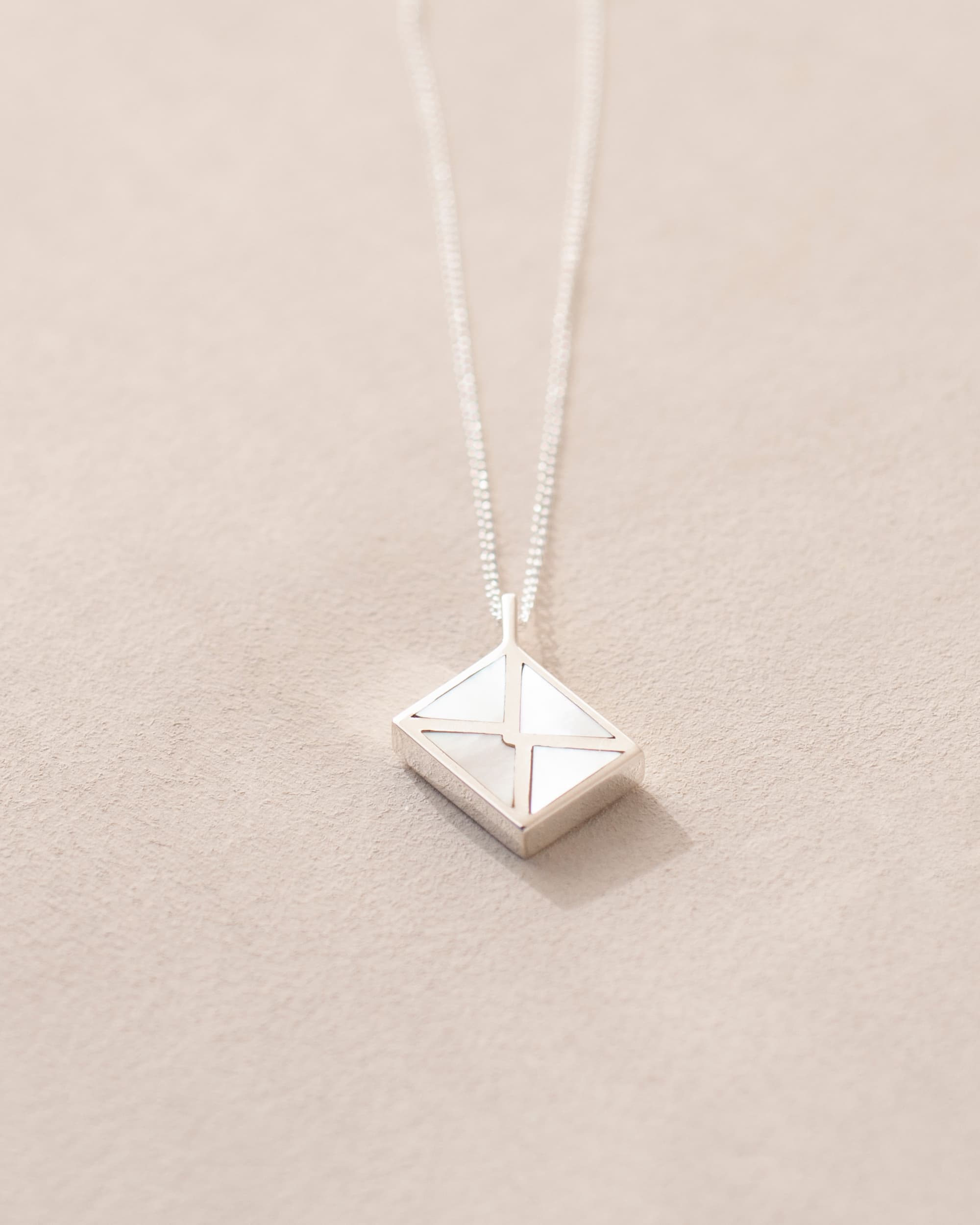 A silver charm shaped like an envelope with mother of pearl dangling from a chain, on a light background.