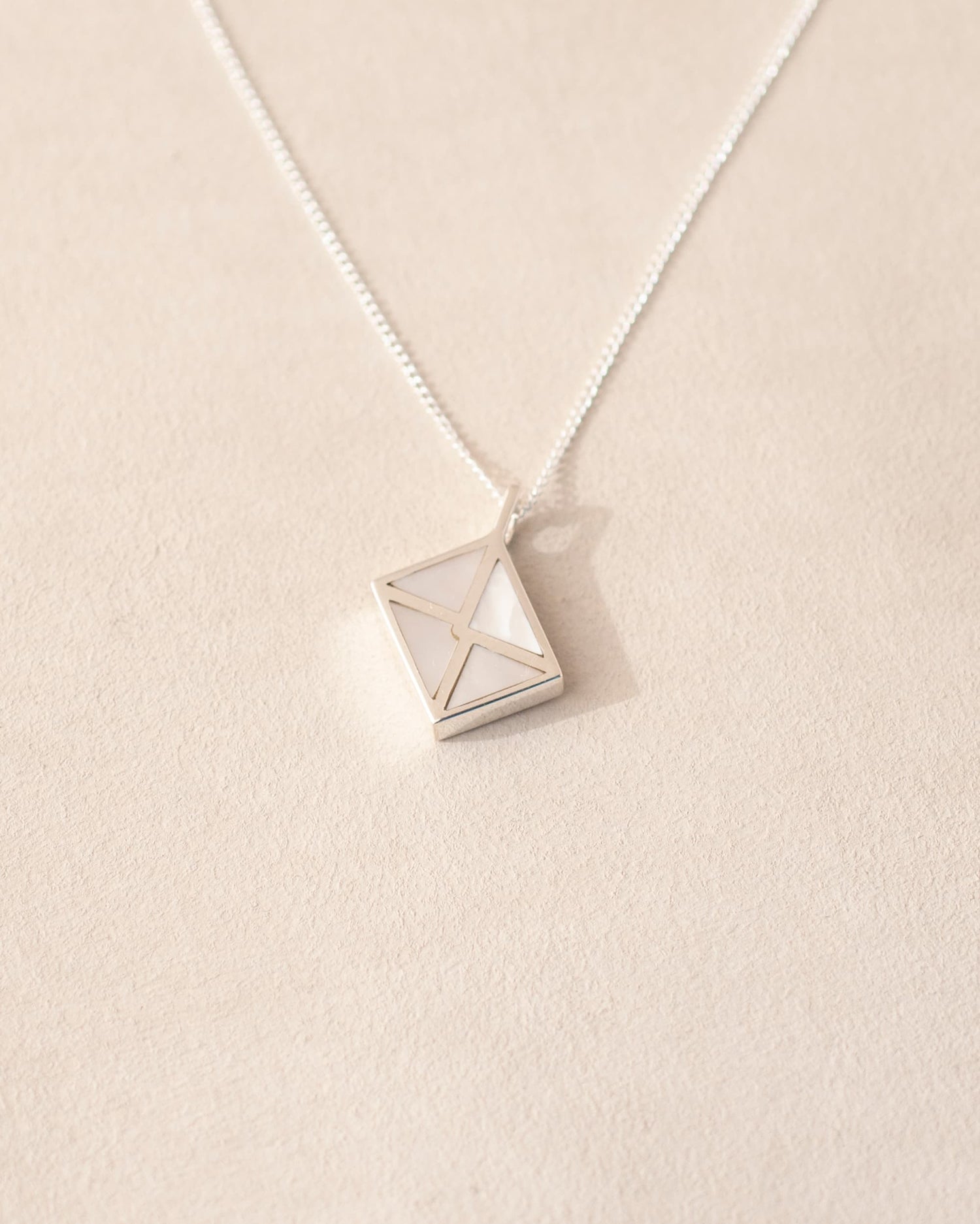 A silver charm shaped like an envelope with mother of pearl dangling from a chain, on a light background.