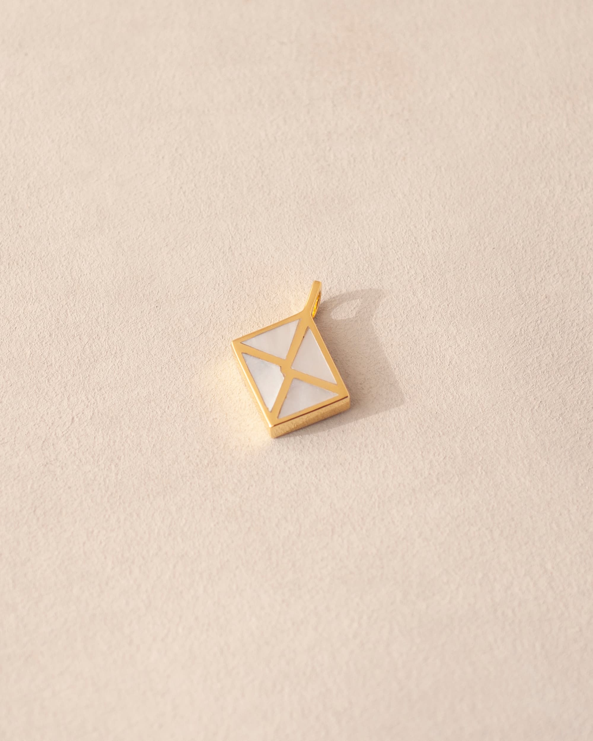 A gold vermeil envelope charm with mother of pearl inlay on a beige background