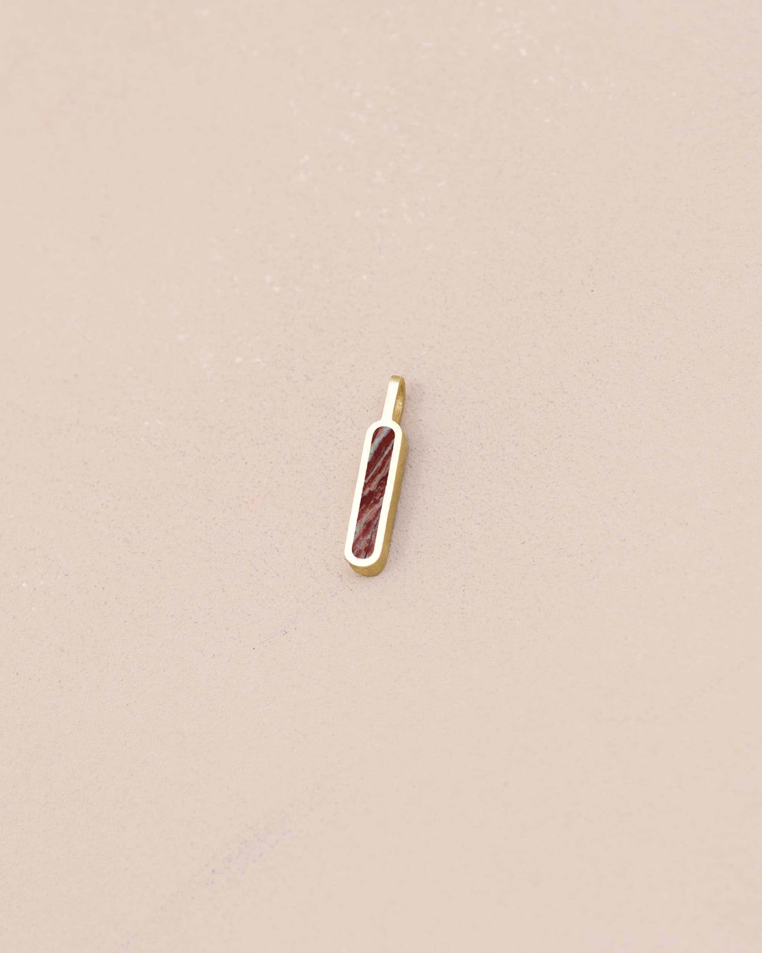 Gold pendant with a red stone on a beige background