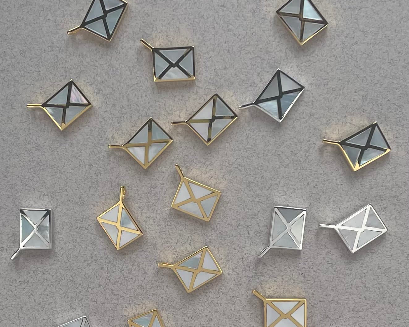 many silver and gold envelope charms inlayed with mother of pearl laying on a textured background