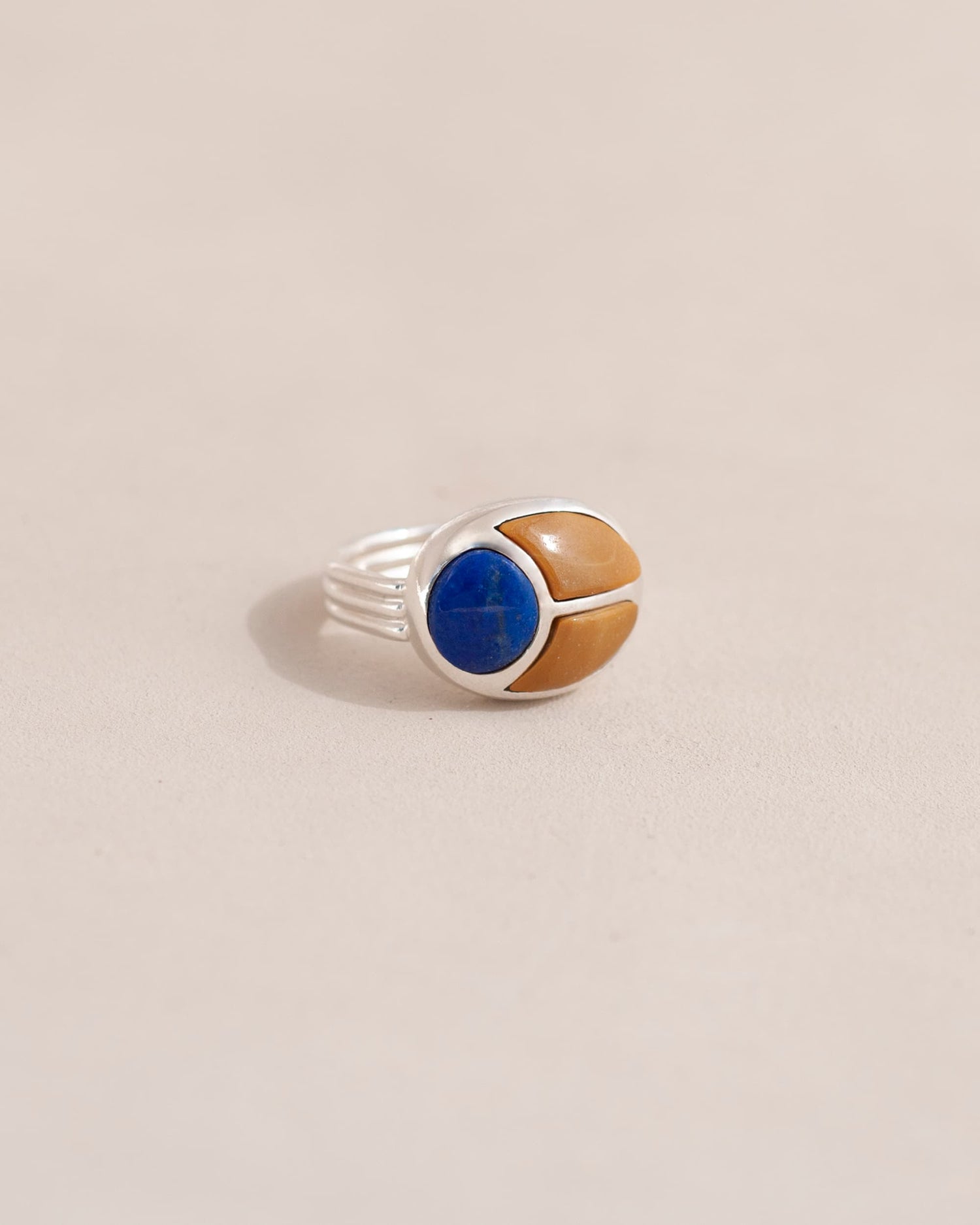 A silver ring featuring a scarab design with lapis lazuli and yellow opal inlays, displayed against a neutral background.