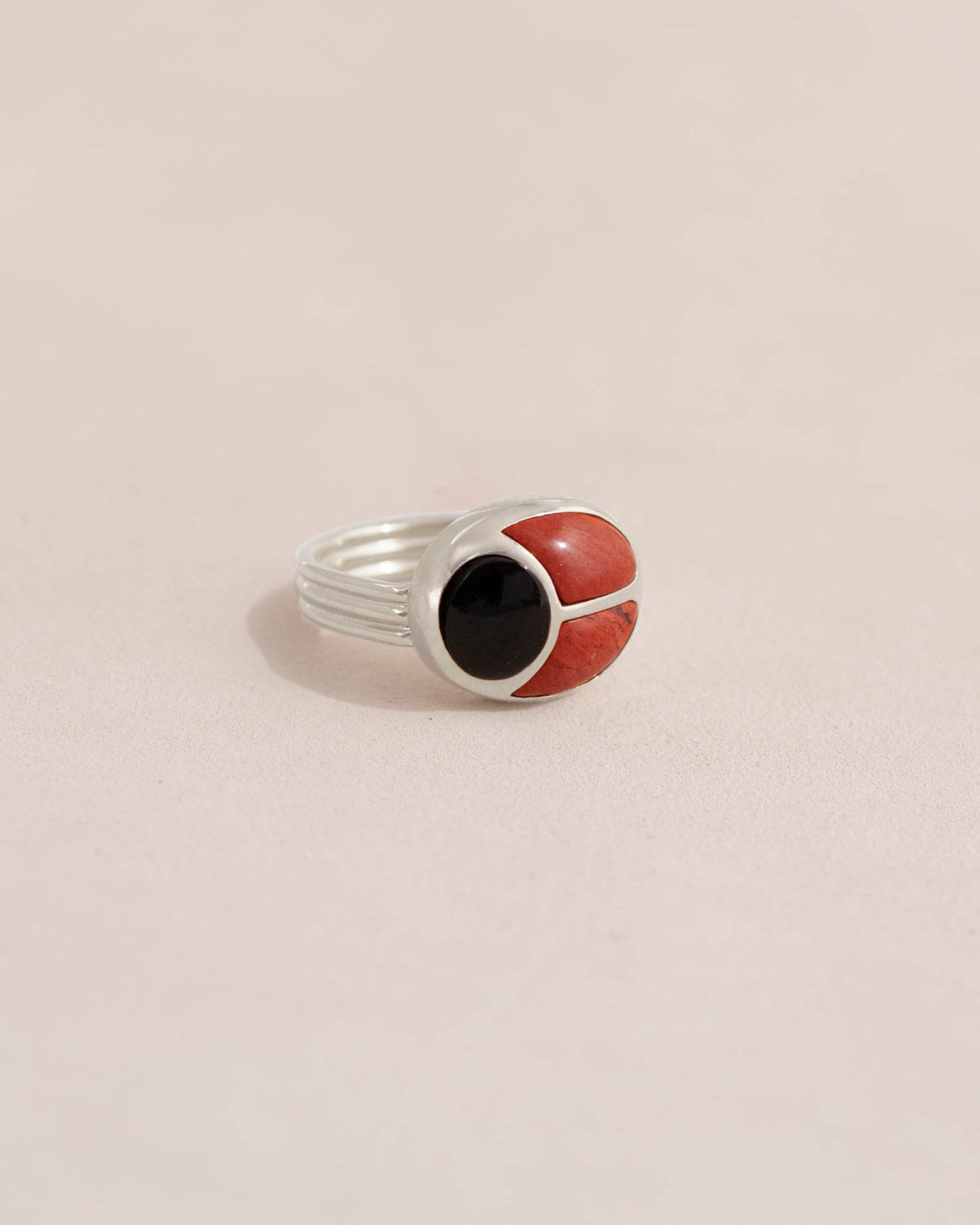 A silver ring featuring a scarab design with onyx and red jasper inlays, displayed against a neutral background.