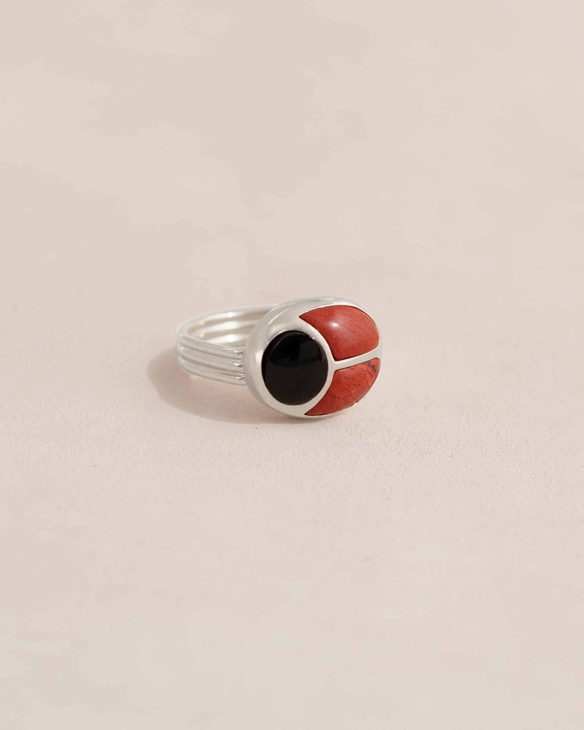 A silver ring featuring a scarab design with onyx and red jasper inlays, displayed against a neutral background.