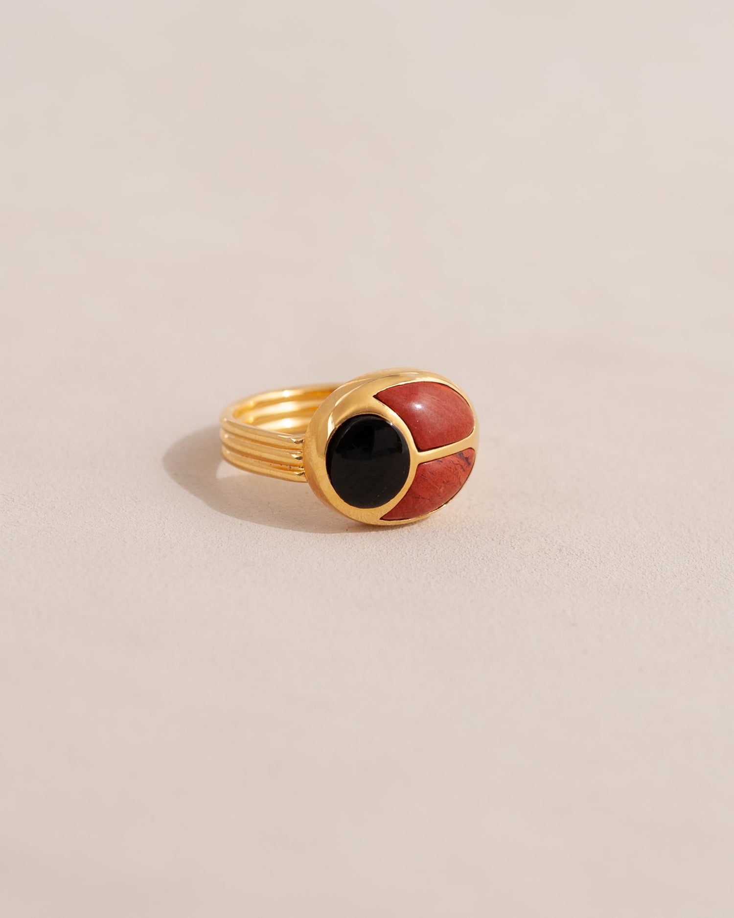 A gold ring featuring a scarab design with onyx and red jasper inlays, displayed against a neutral background.