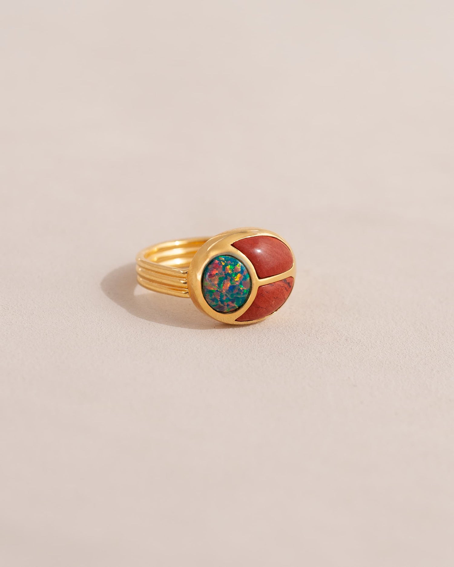 A gold ring featuring a scarab design with starry opal and red jasper inlays, displayed against a neutral background.