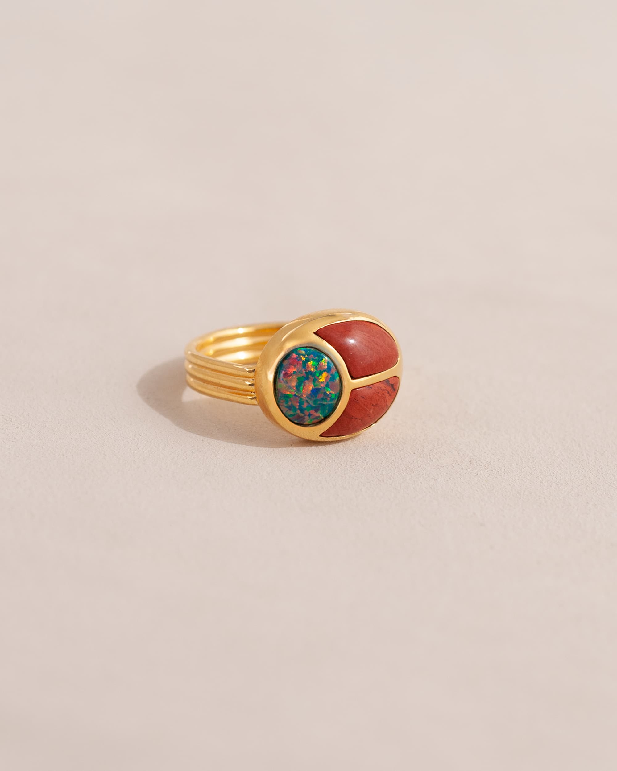 A gold ring featuring a scarab design with starry opal and red jasper inlays, displayed against a neutral background.