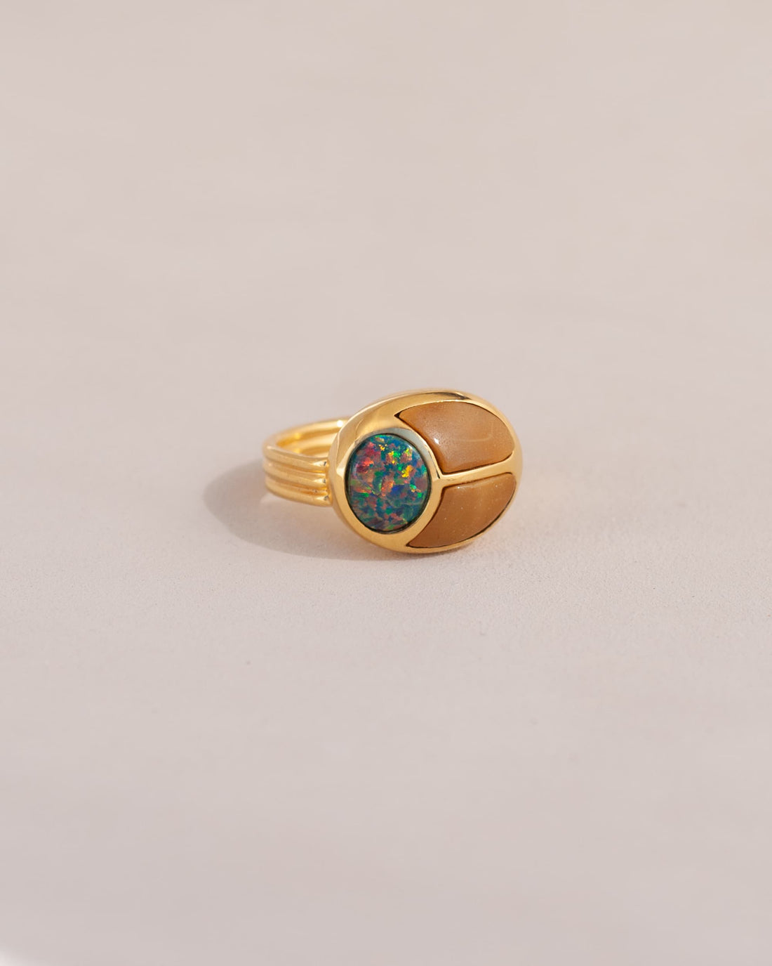 A gold ring featuring a scarab design with starry opal and yellow opal inlays, displayed against a neutral background.