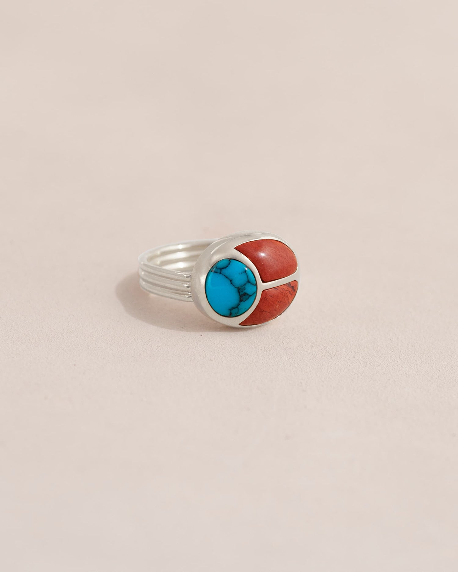 A silver ring featuring a scarab design with turquoise and red jasper inlays, displayed against a neutral background.