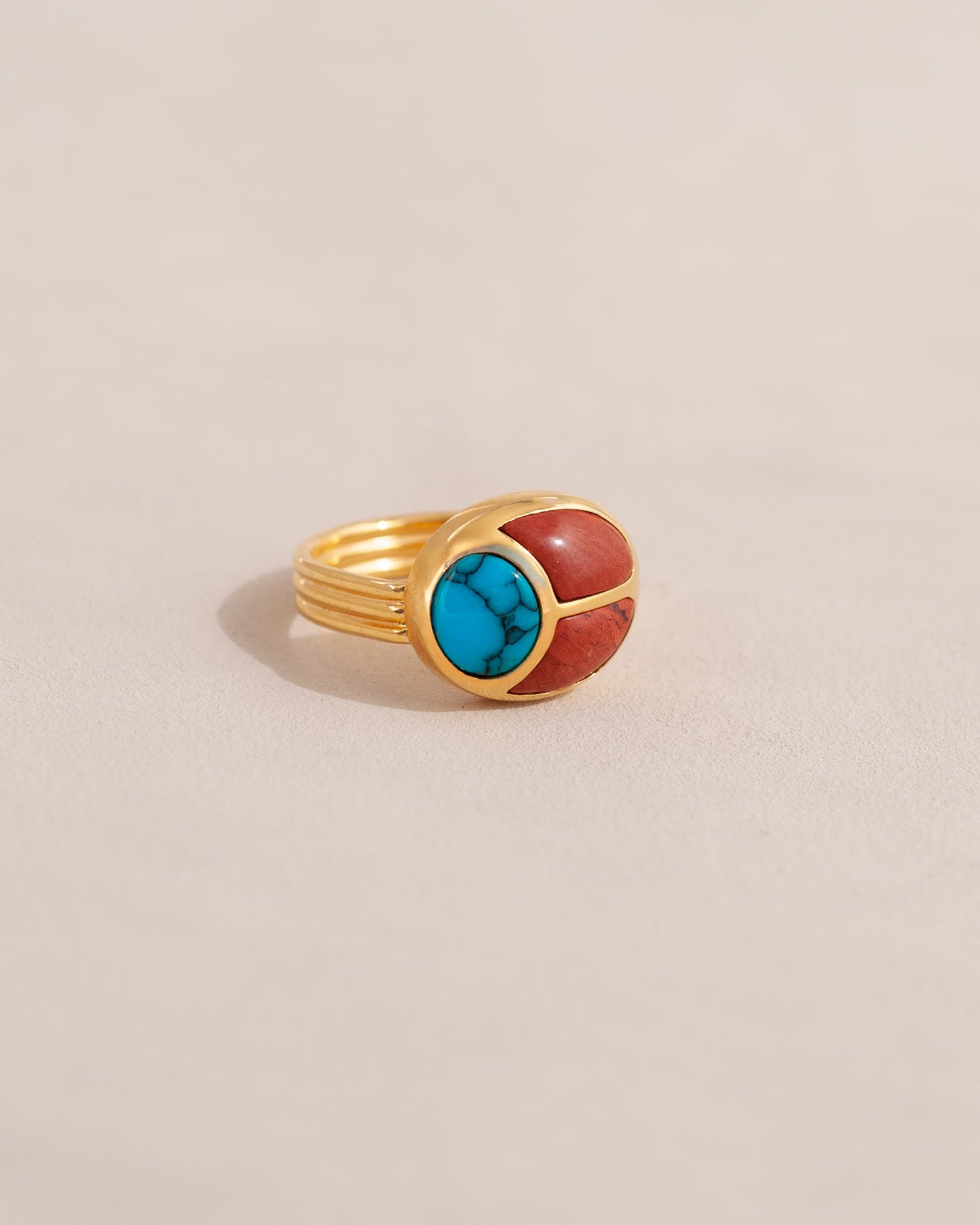 A gold ring featuring a scarab design with turquoise and red jasper inlays, displayed against a neutral background.