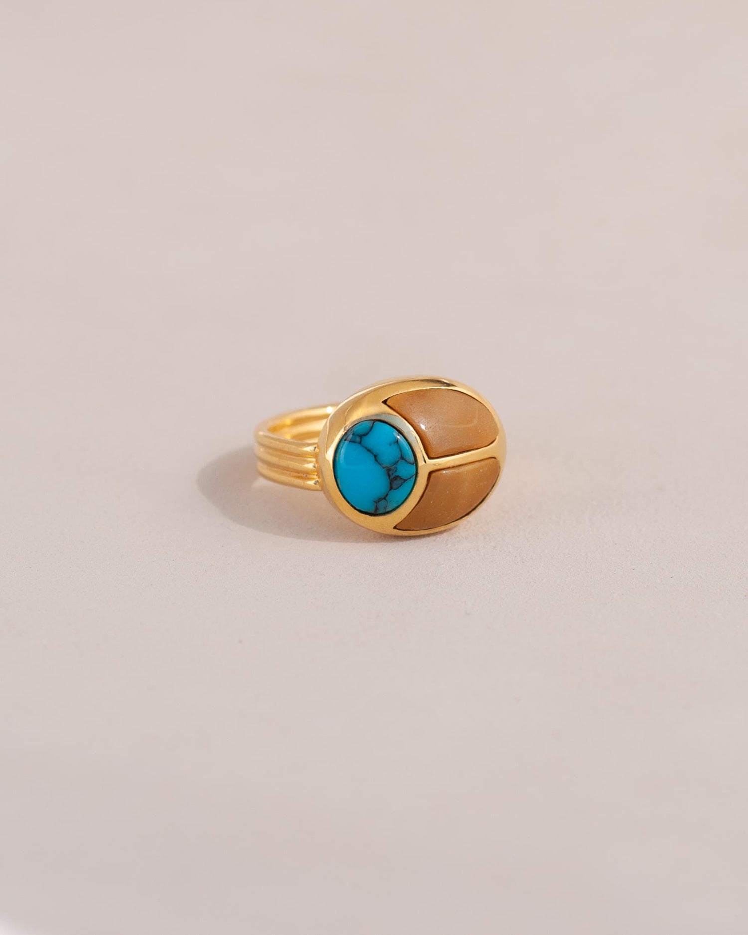 A gold ring featuring a scarab design with turquoise and yellow opal inlays, displayed against a neutral background.