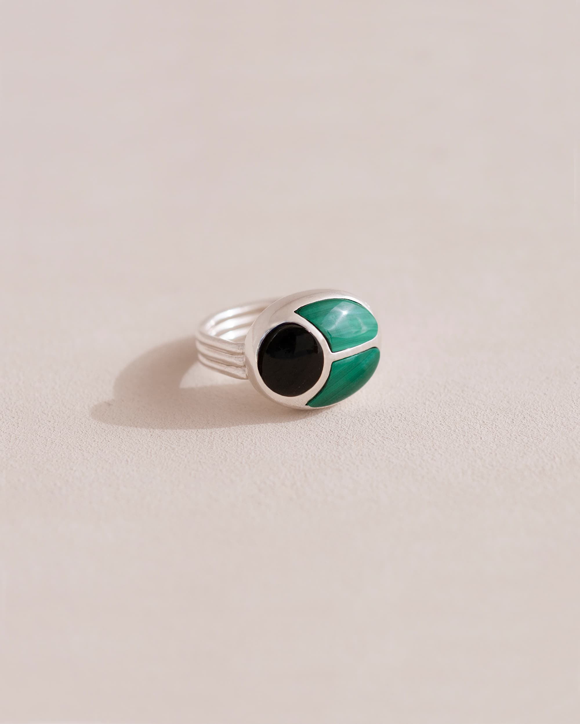 A silver ring featuring a central onyx stone flanked by malachite stones on either side, set against a neutral background.