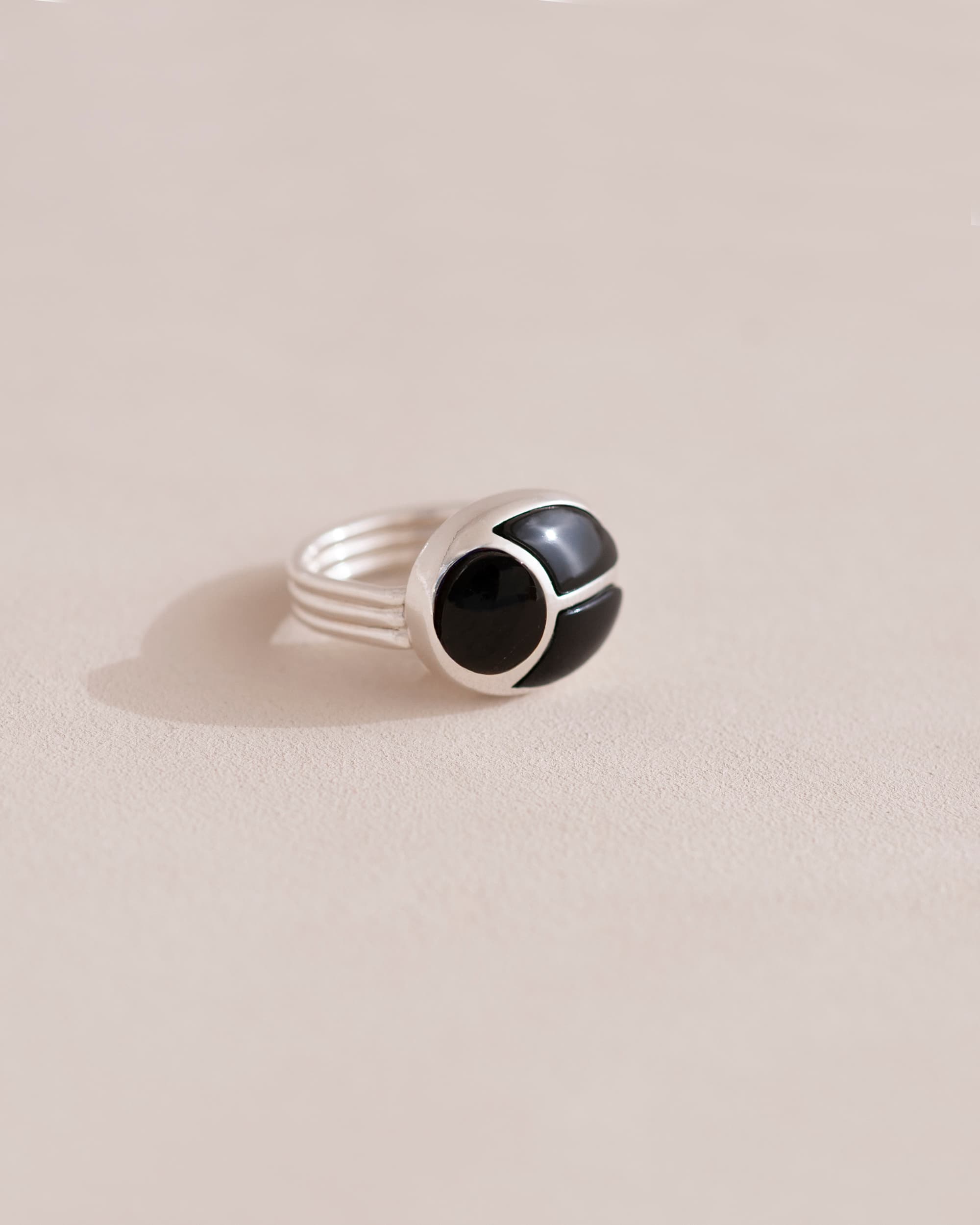 A silver ring featuring a central onyx stone flanked by onyx stones on either side, set against a neutral background.