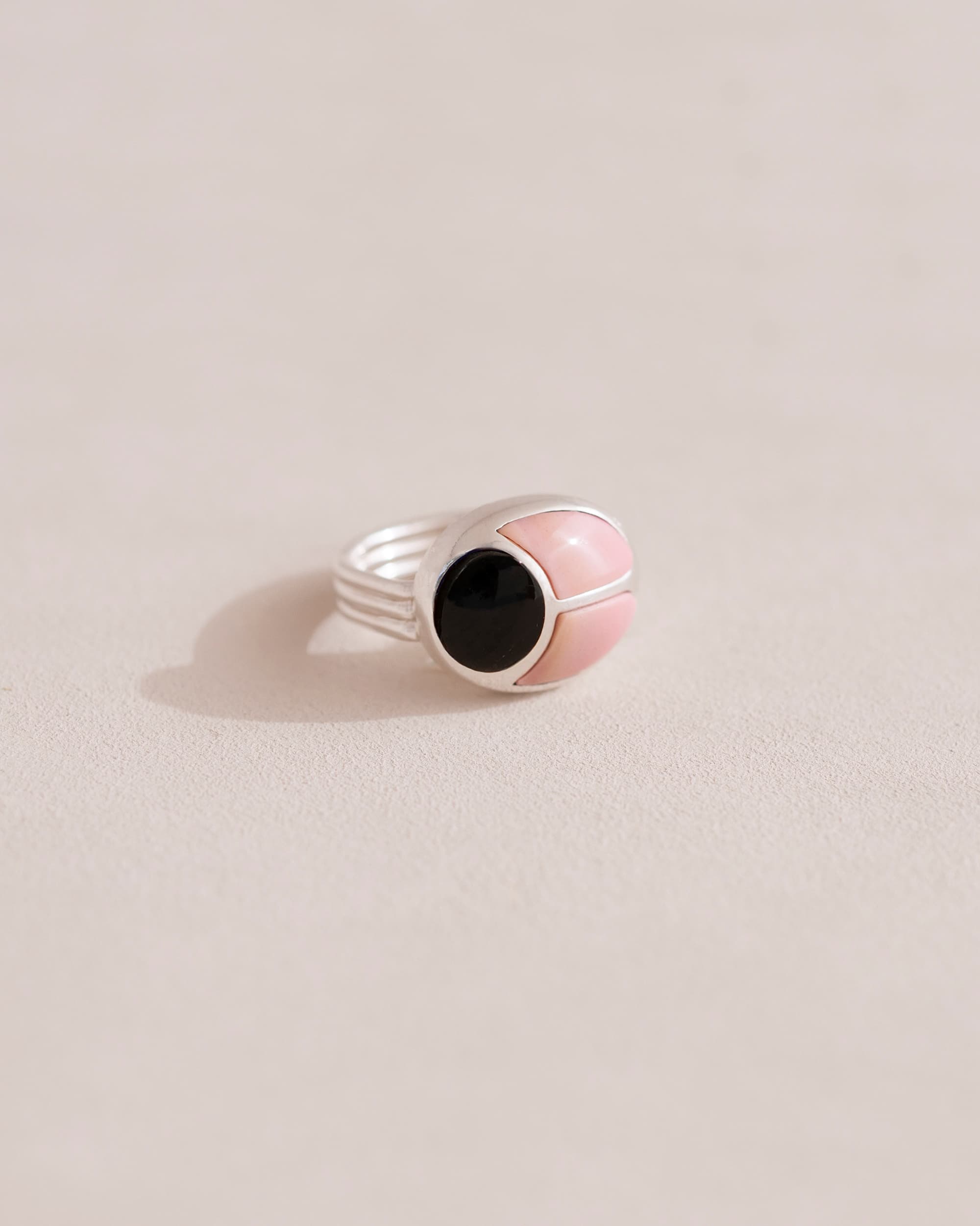 A silver ring with a pink opal center and surrounding onyx, placed on a plain background.
