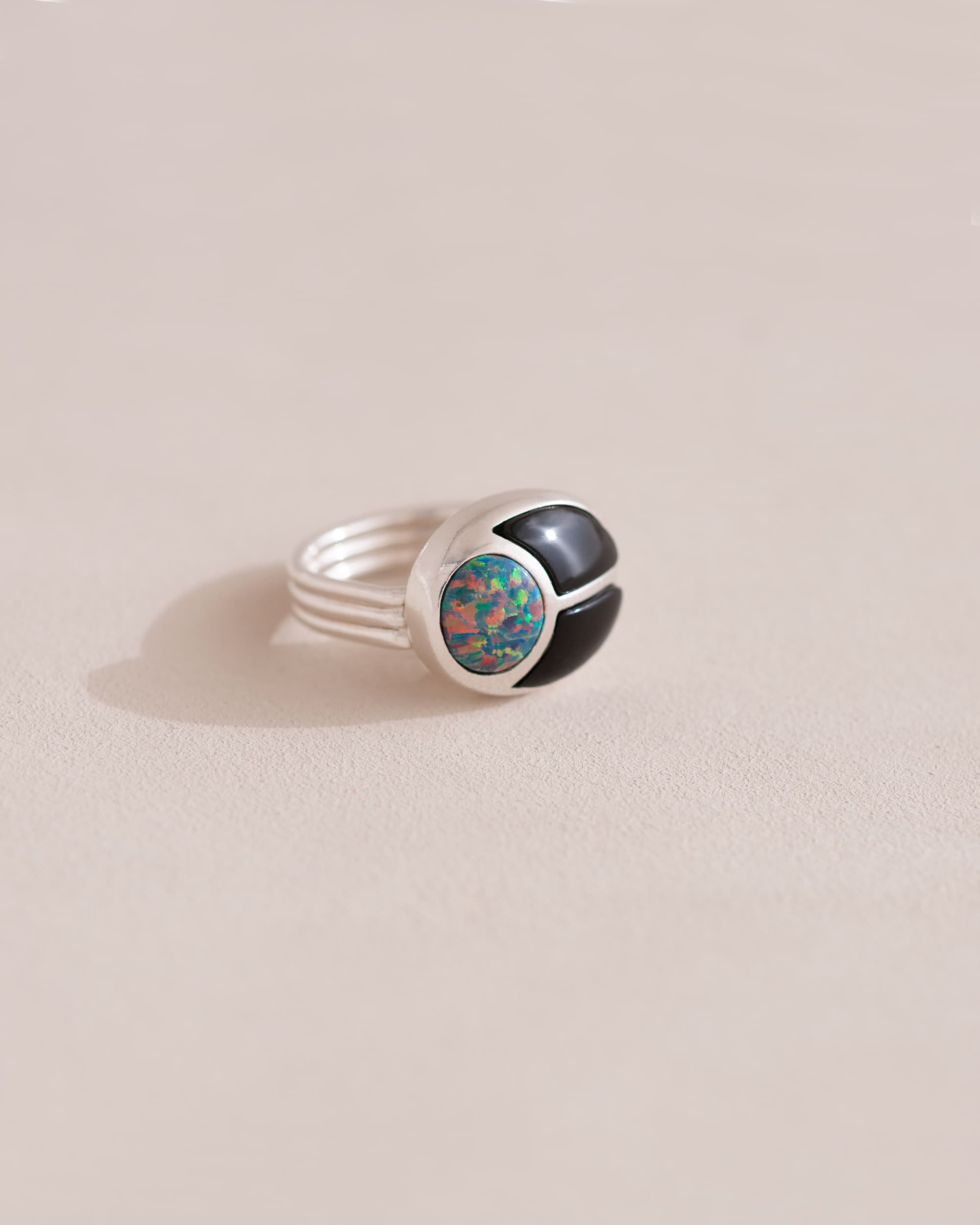 A silver ring featuring a central opal stone flanked by onyx stones on either side, set against a neutral background.