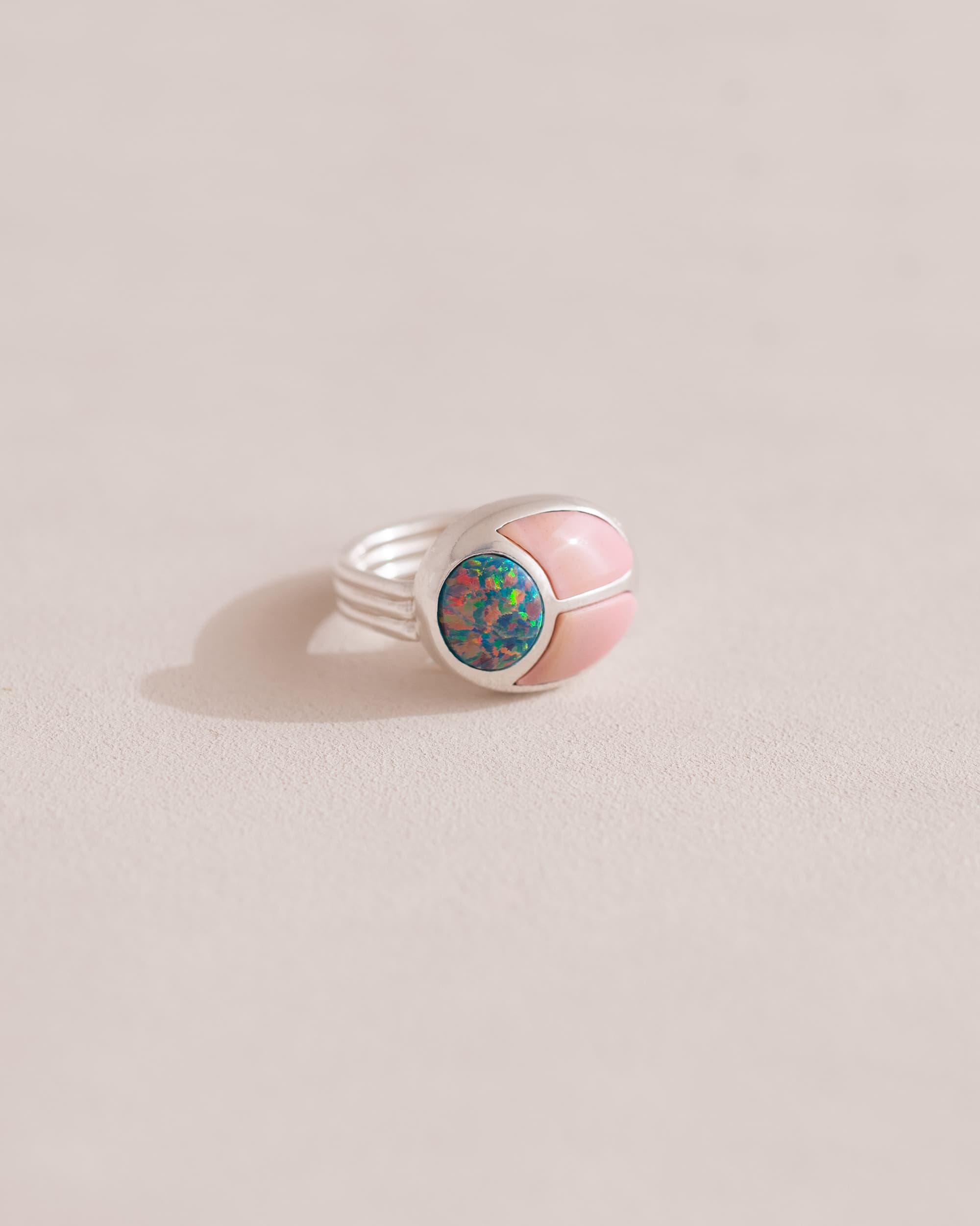 A silver ring featuring a central opal stone flanked by pink opal stones on either side, set against a neutral background.