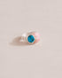 A silver ring featuring a central turquoise stone flanked by pink opal stones on either side, set against a neutral background.