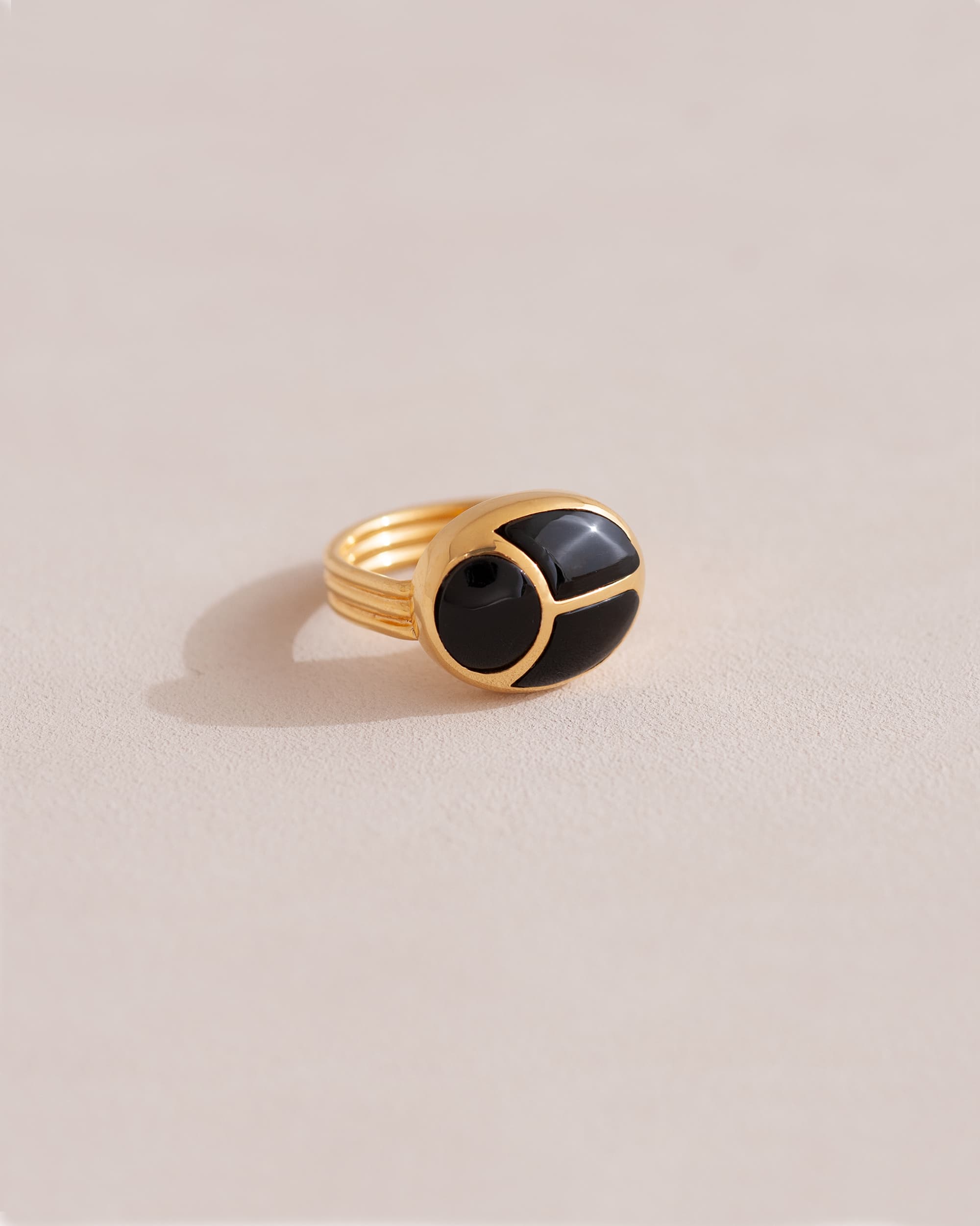 A gold ring featuring a central onyx stone flanked by onyx stones on either side, set against a neutral background.