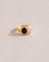 A gold ring featuring a central onyx stone flanked by pink opal stones on either side, set against a neutral background.