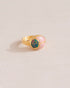 A gold ring featuring a central opal stone flanked by pink opal stones on either side, set against a neutral background.