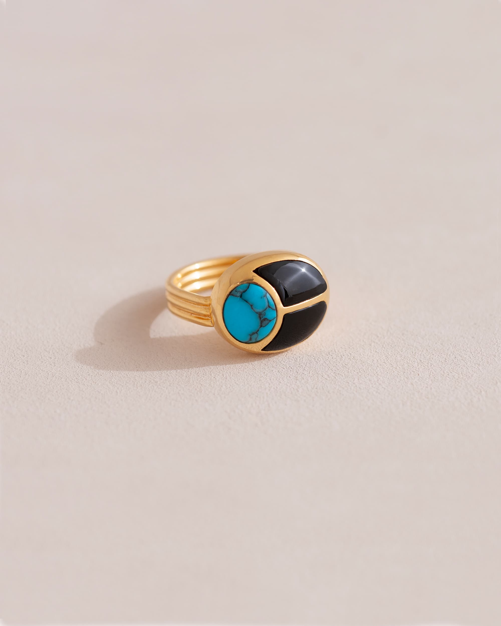 A gold ring featuring a central turquoise stone flanked by onyx stones on either side, set against a neutral background.