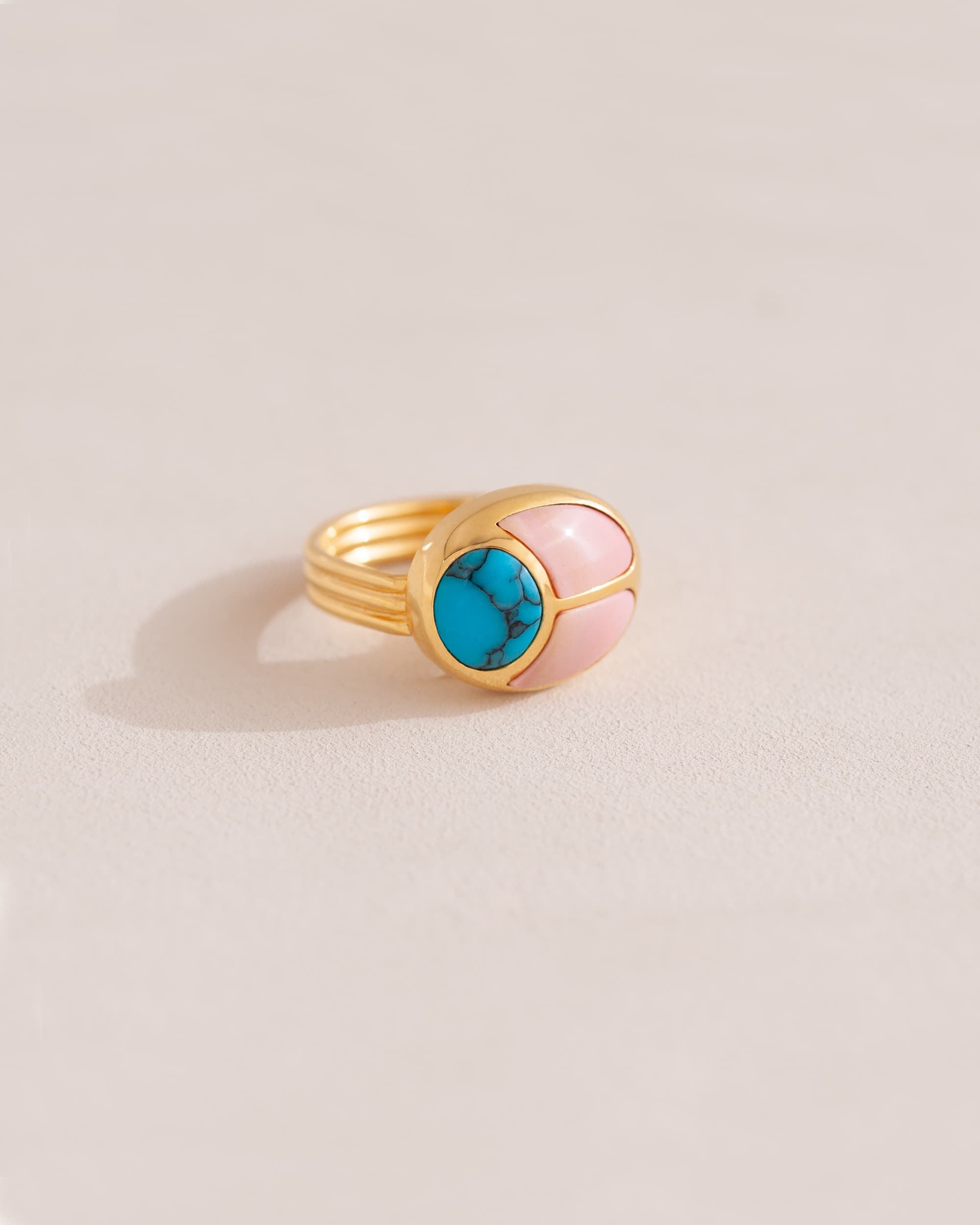 A 14K yellow gold ring with a turquoise and pink opal stone set in a gold band.