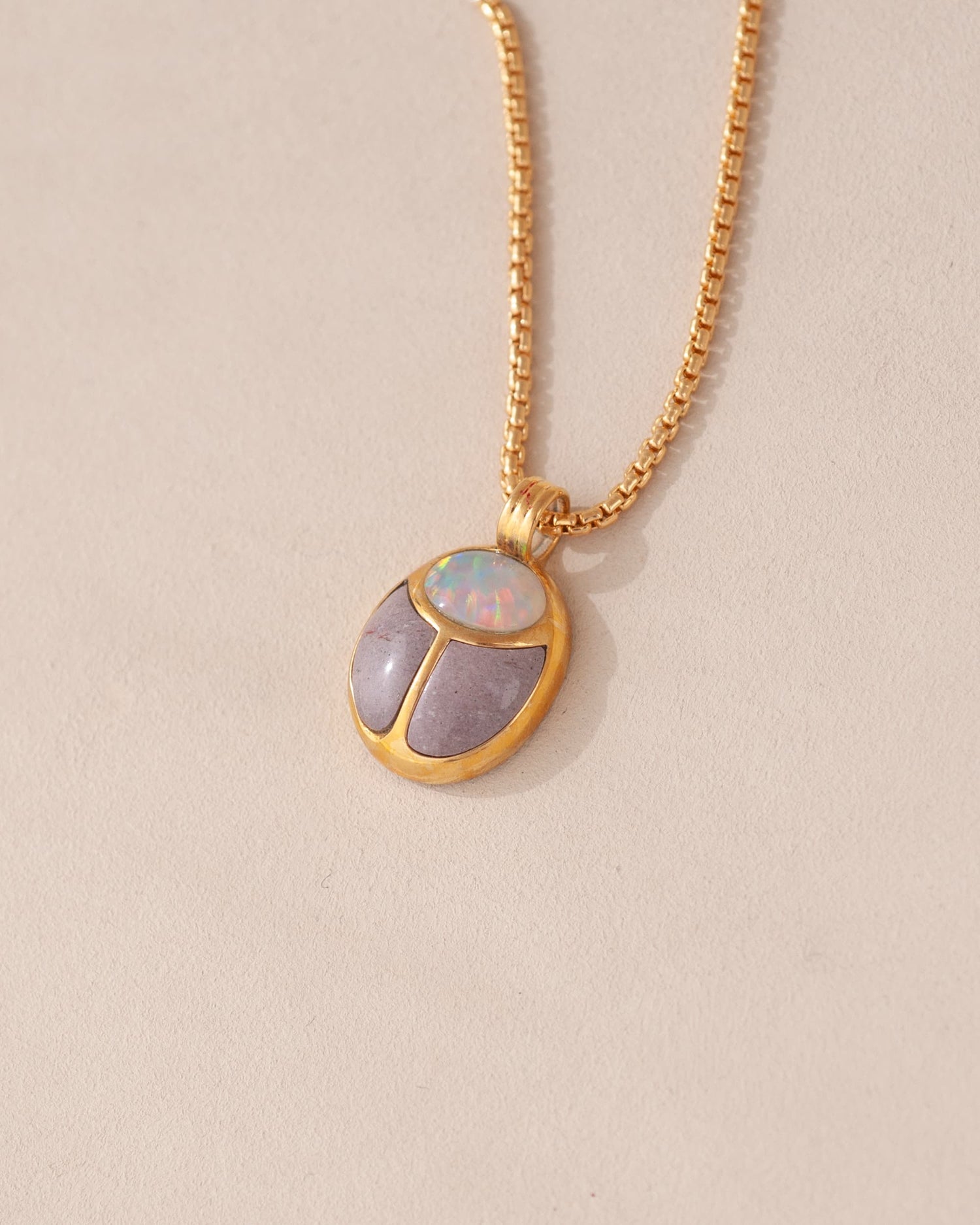 A gold vermeil necklace featuring a scarab amulet pendant with inlays of purple and white stones, displayed against a neutral background.