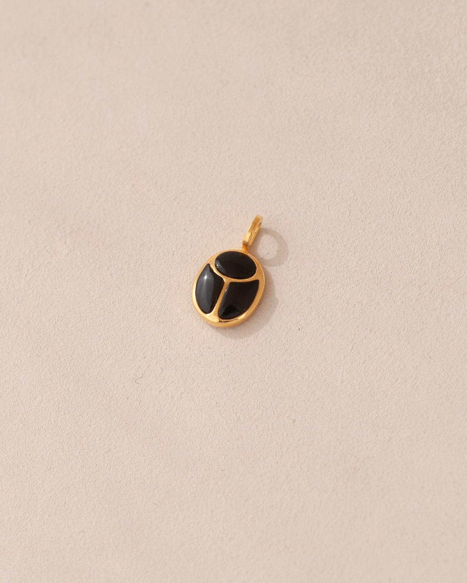 A gold charm featuring a scarab design with onyx inlays, displayed against a neutral background.