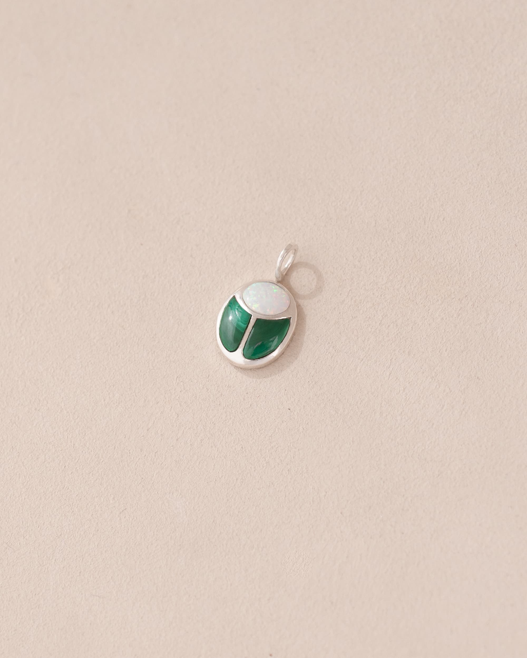 A silver charm featuring a miniature scarab amulet design with jelly opal and malachite inlay, displayed against a neutral background.