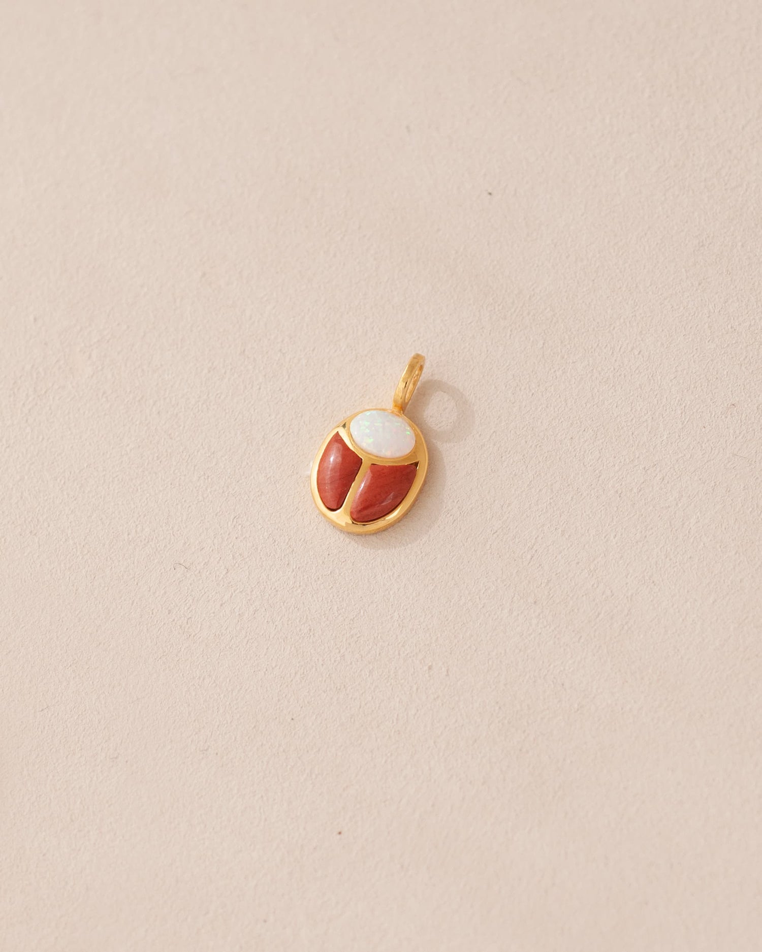 A small gold charm featuring a red jasper and opal scarab design.