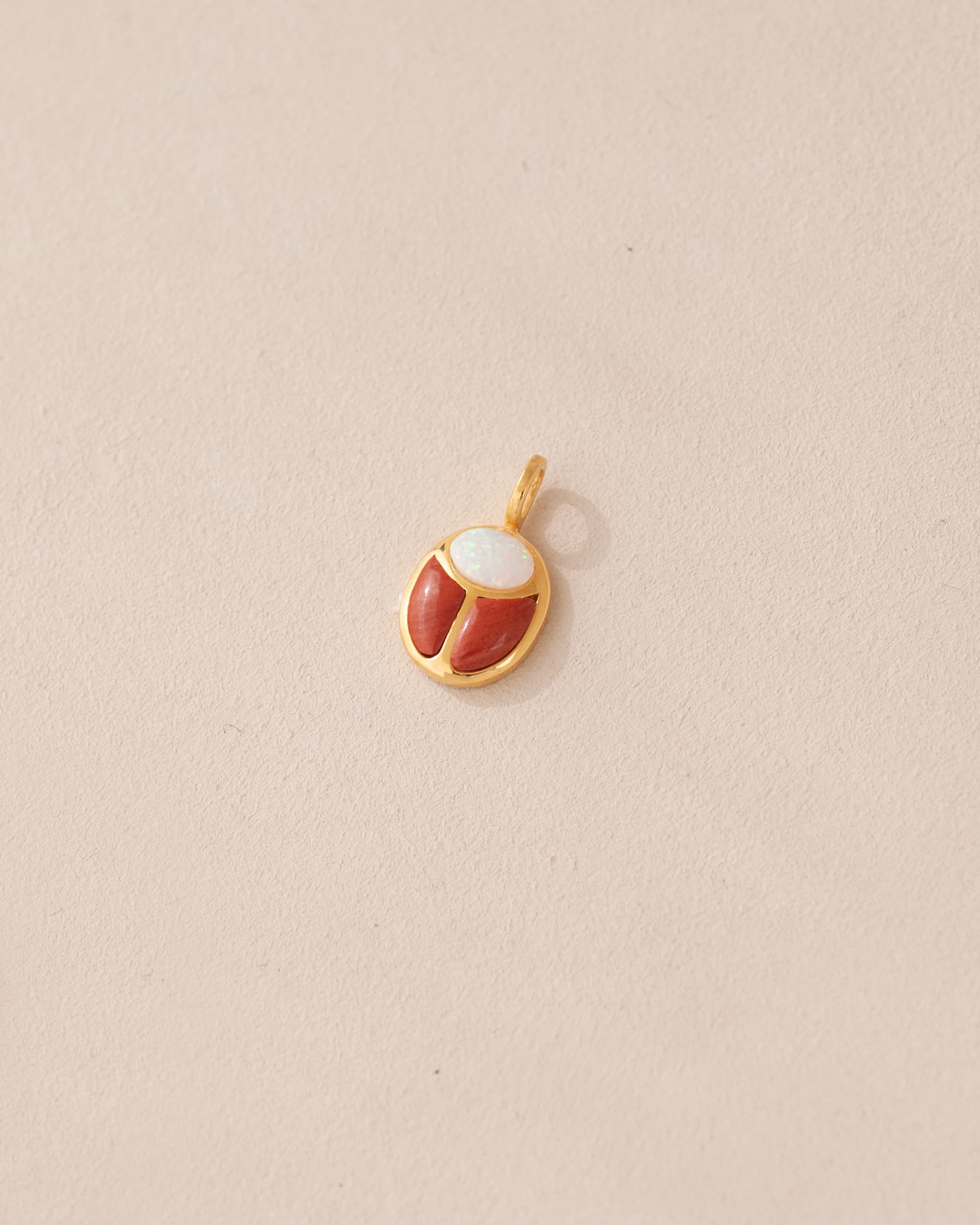A small gold charm featuring a red jasper and opal scarab design.