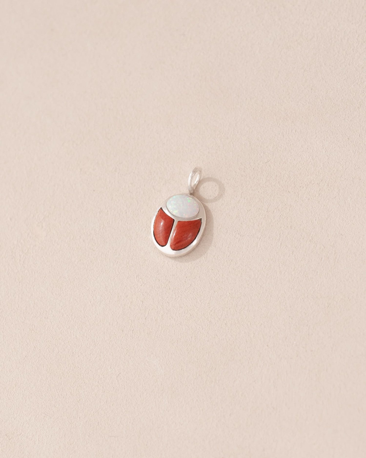 A small silver charm featuring a red jasper and opal scarab design.