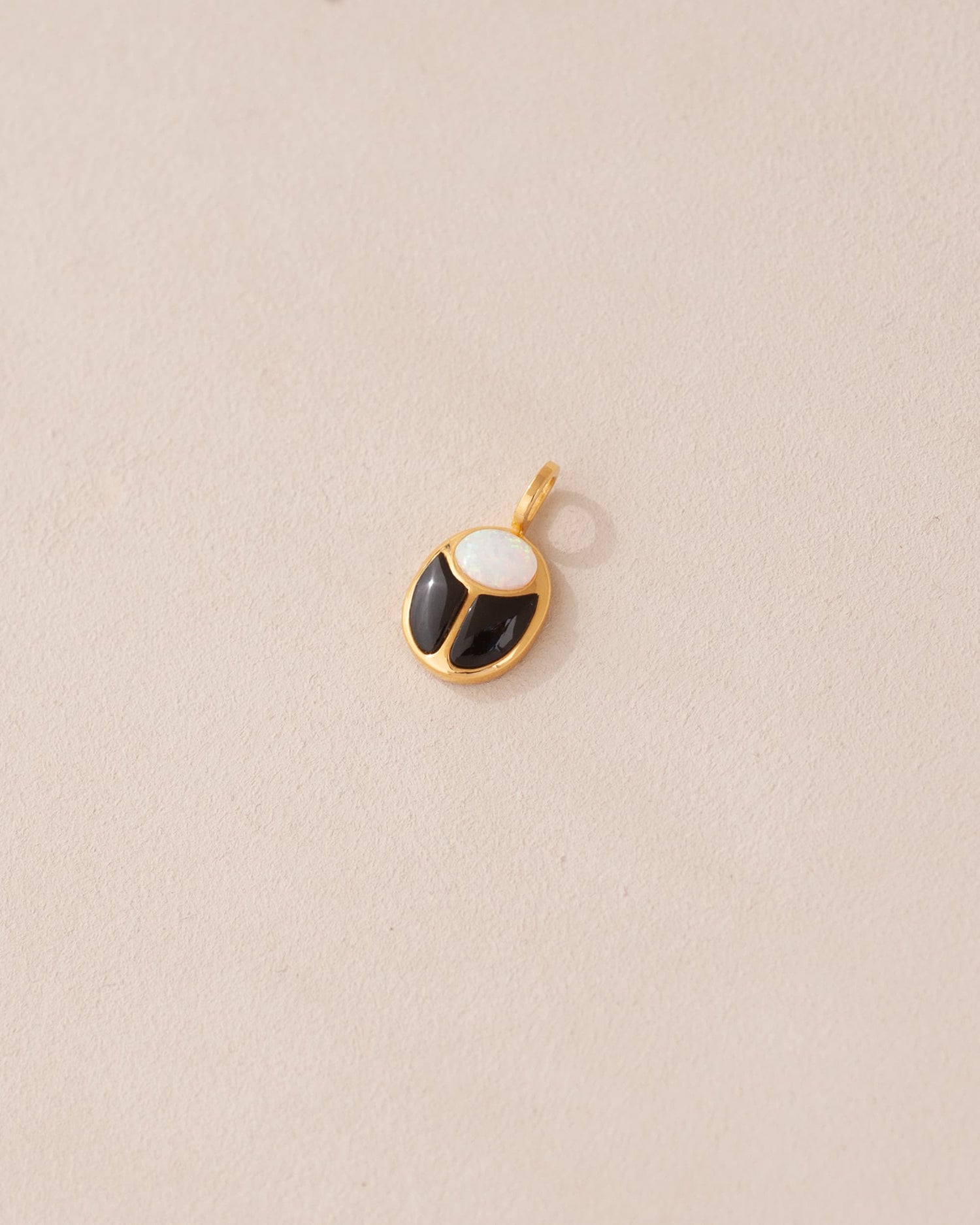 A small gold charm featuring a black and white opal scarab design.