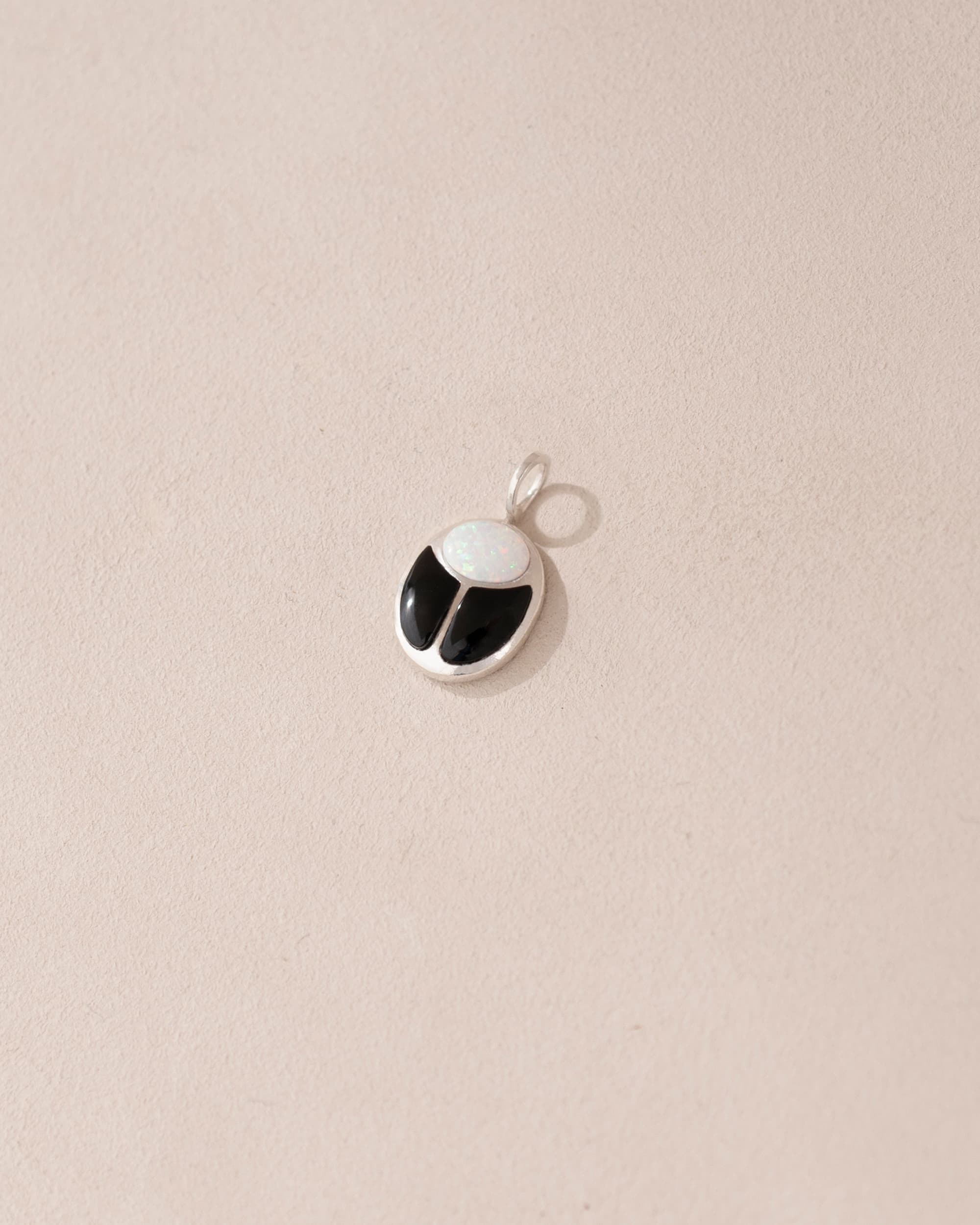 A small silver charm featuring a black and white stone, likely an onyx, designed to resemble a scarab amulet.