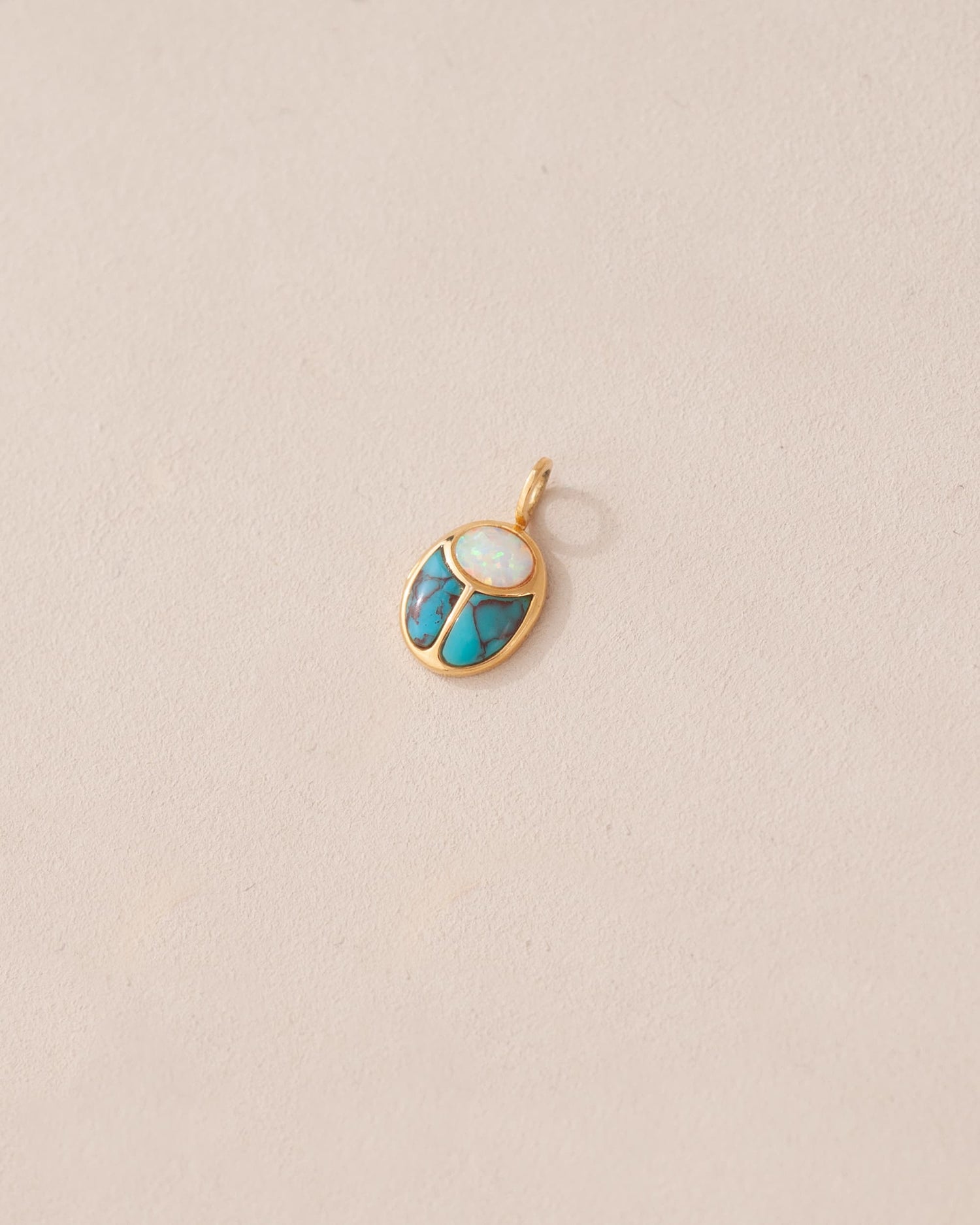 A small gold charm featuring a scarab design with opal and turquoise inlays, displayed against a neutral background.