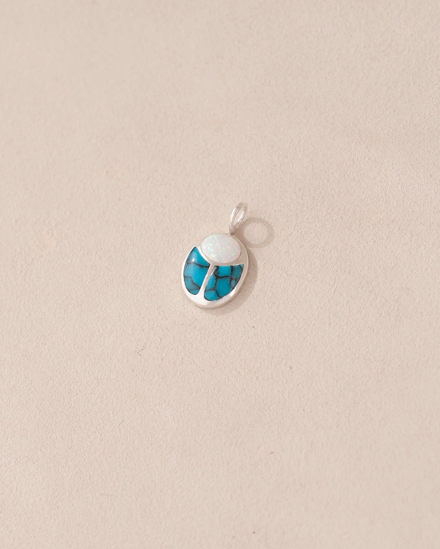 A small silver charm featuring a blue and white stone, designed to resemble a scarab amulet.