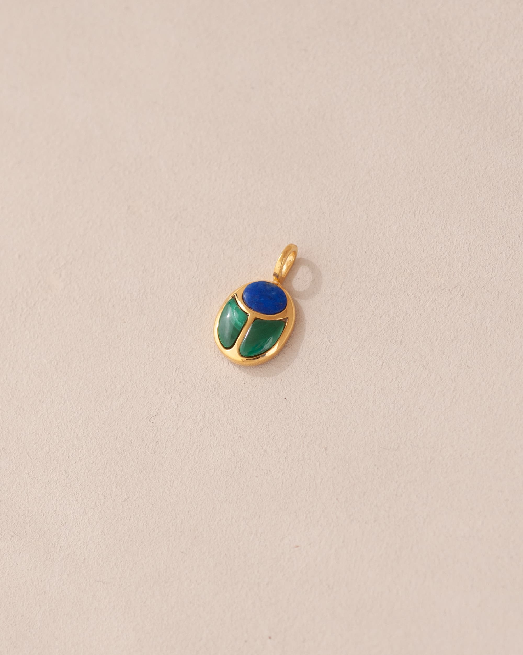 A gold charm featuring a scarab design with lapis lazuli and malachite inlays, displayed against a neutral background.