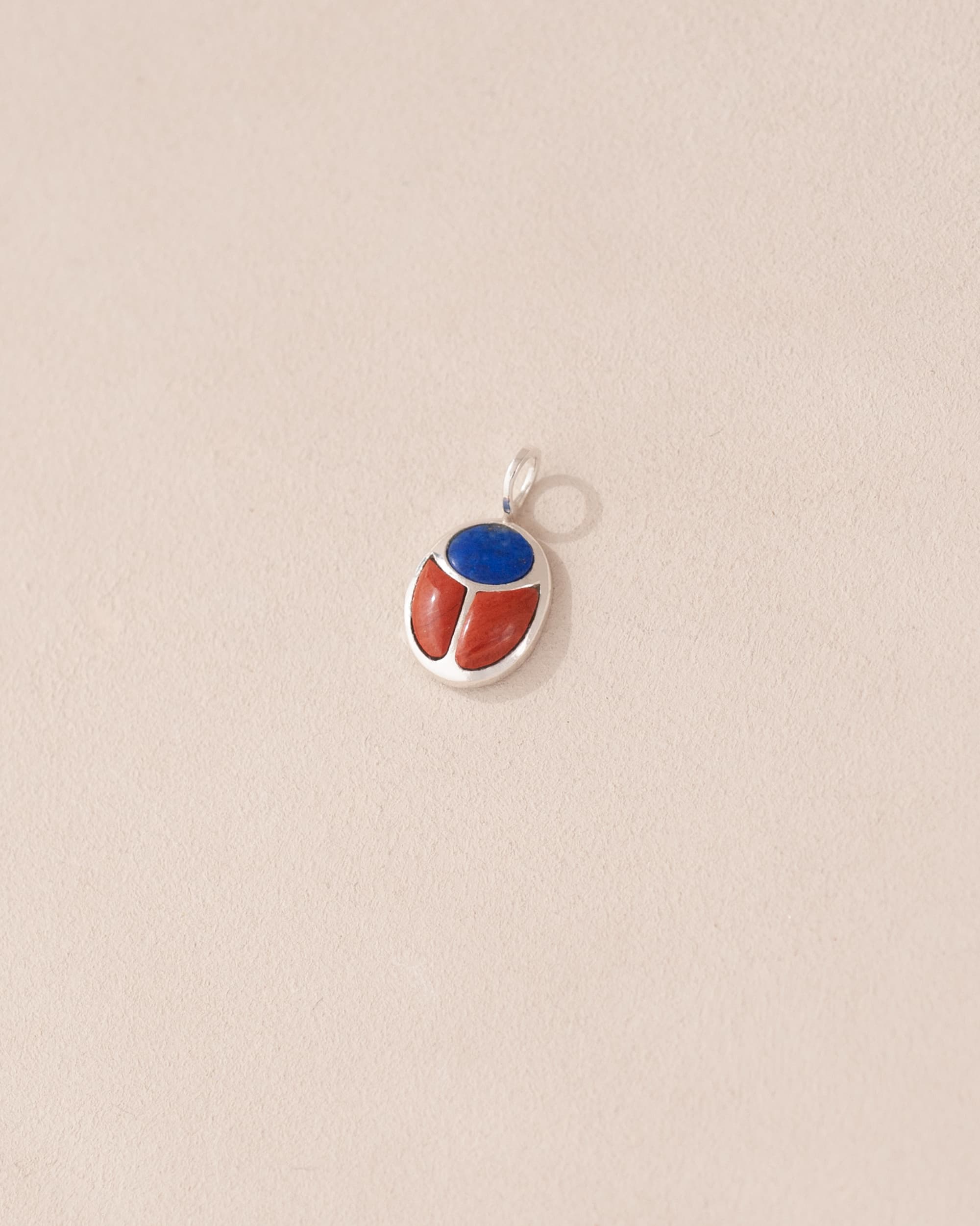 A silver-colored charm with a lapis lazuli and red jasper design, attached to a small silver chain.