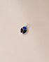 A silver-colored charm with a blue lapis lazuli center and black onyx surround, placed against a beige background.