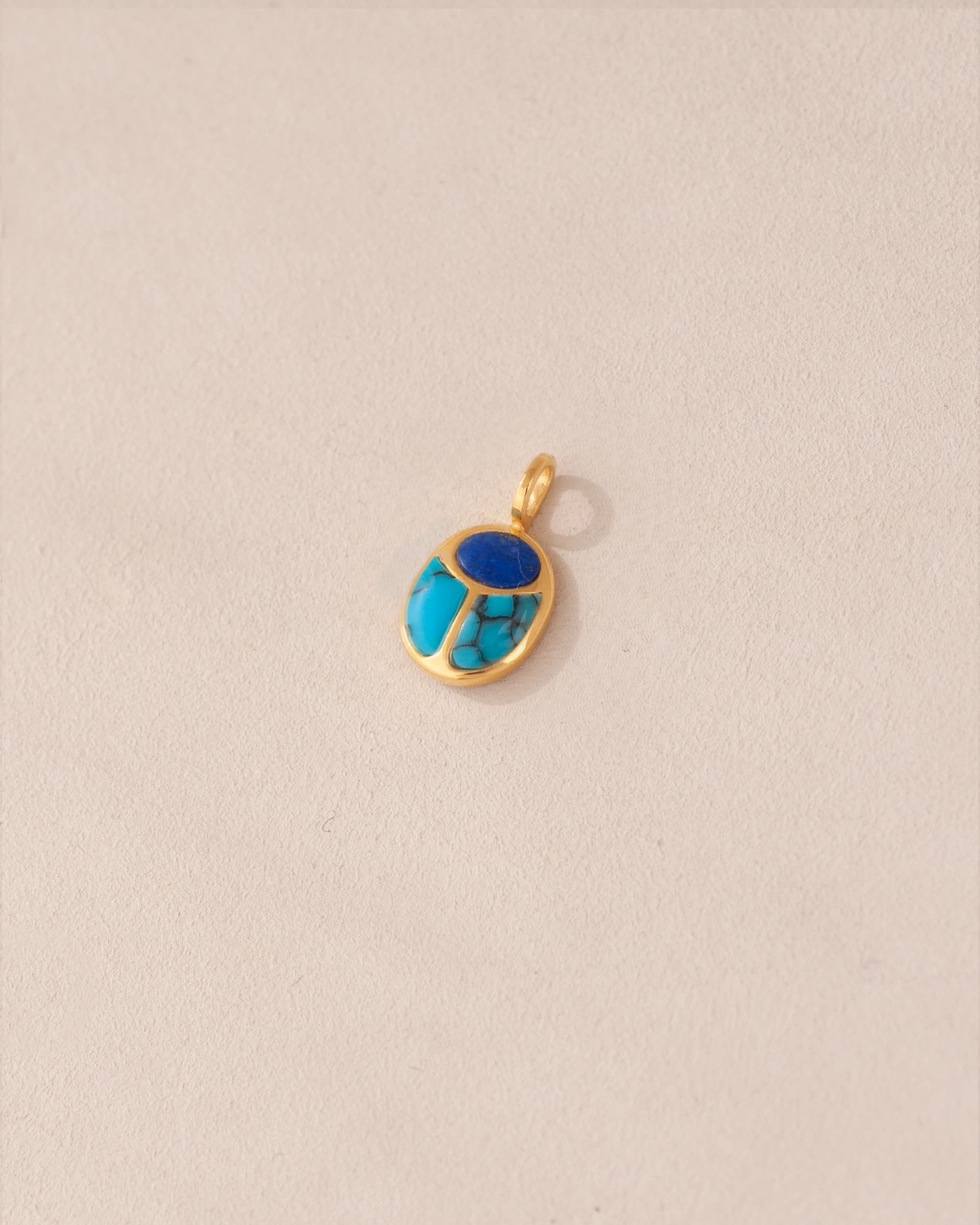 A gold charm featuring a lapis lazuli and turquoise scarab design.