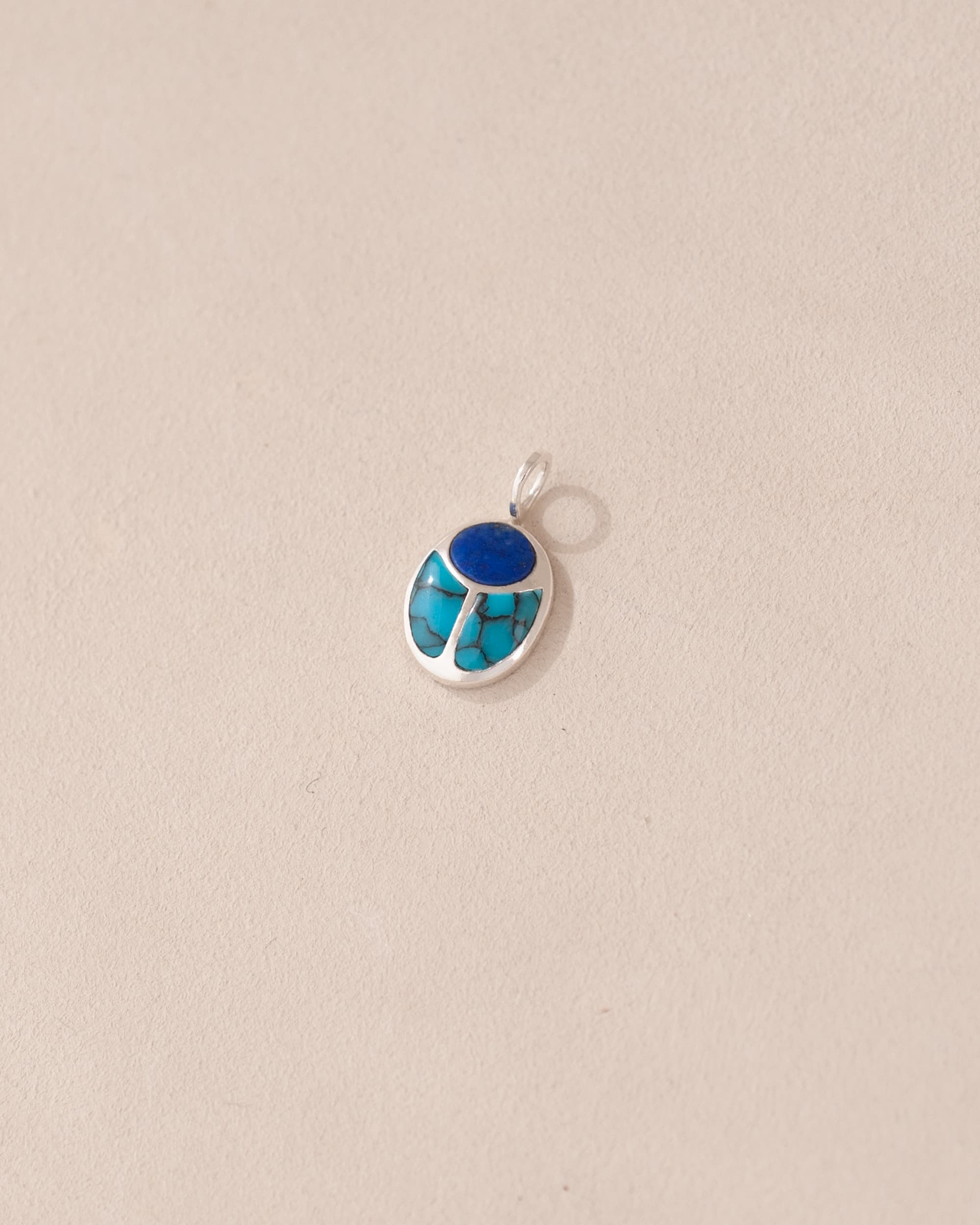 A silver charm featuring a small lapis lazuli and turquoise scarab design.