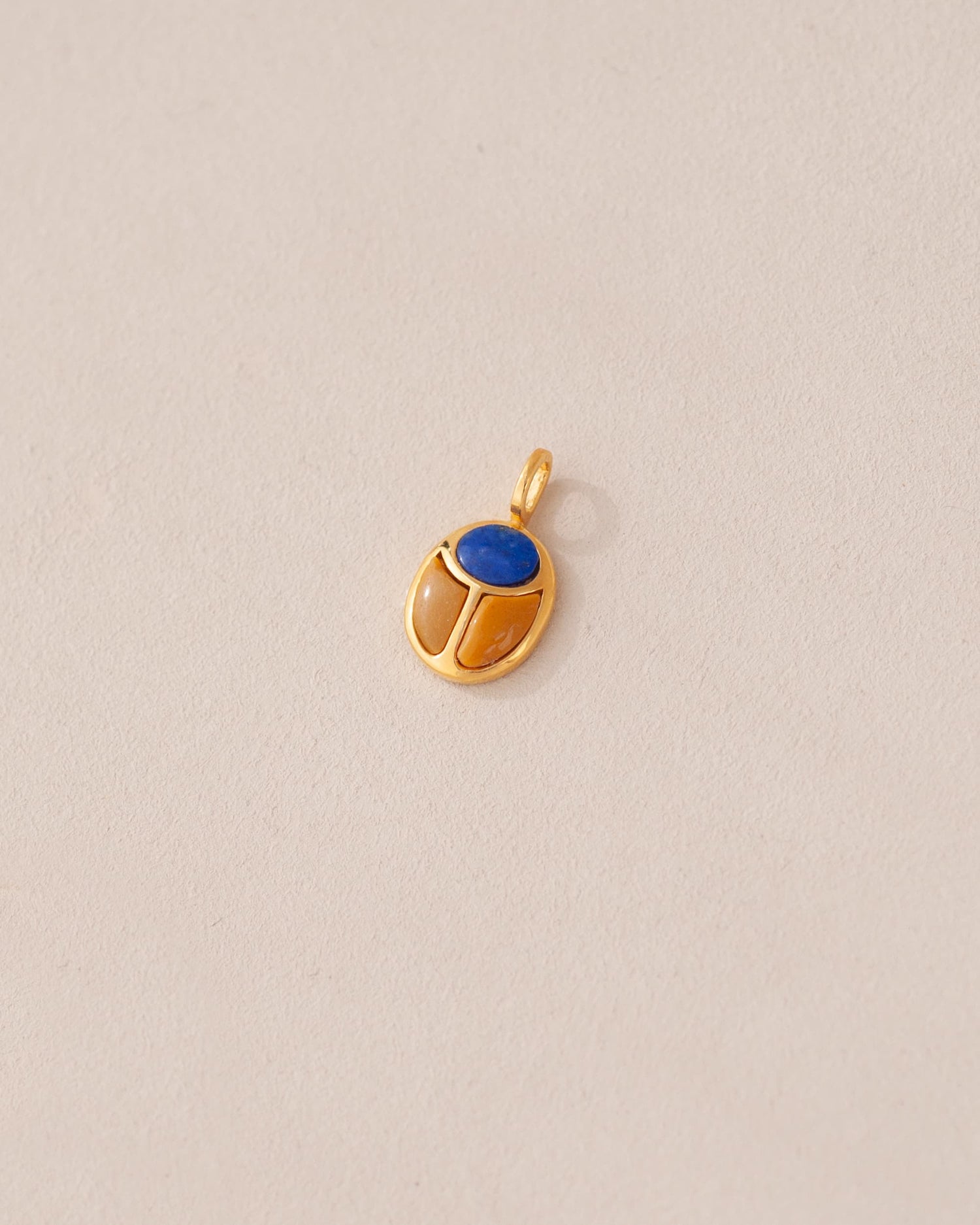 A gold charm featuring a scarab design with a blue lapis lazuli stone in the center, set against a neutral background.