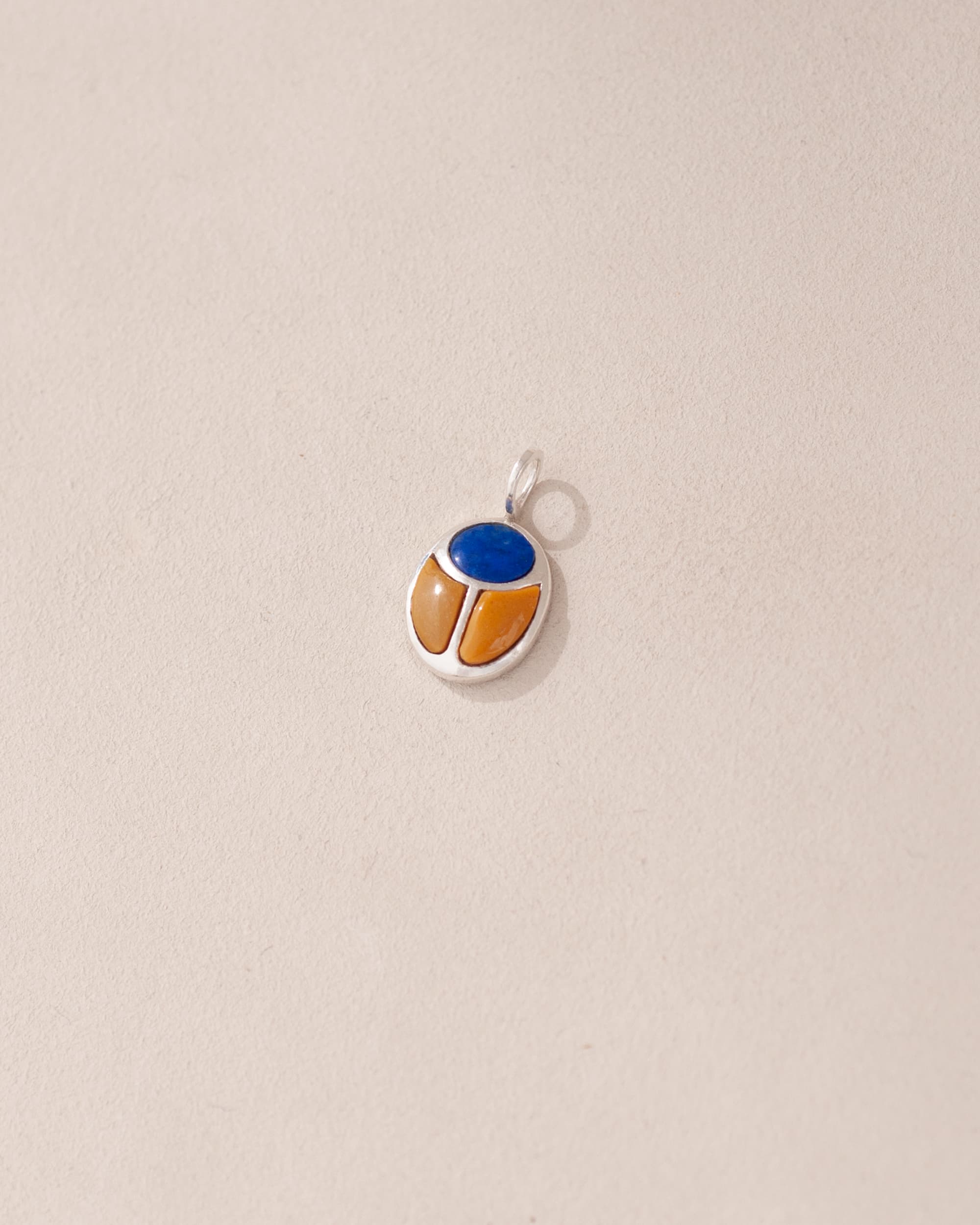 A silver-colored charm with a blue and orange design, possibly representing a scarab amulet.