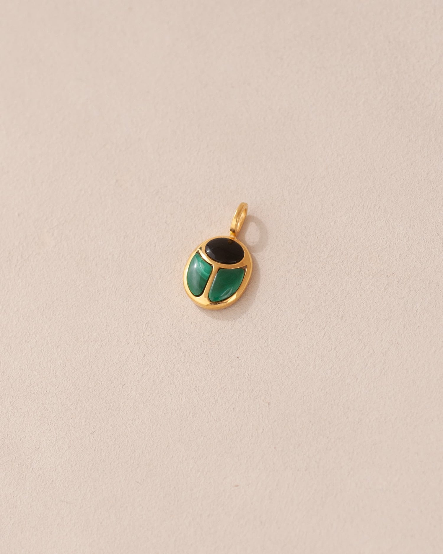 A gold charm featuring a scarab design with onyx and malachite inlays, displayed against a neutral background.