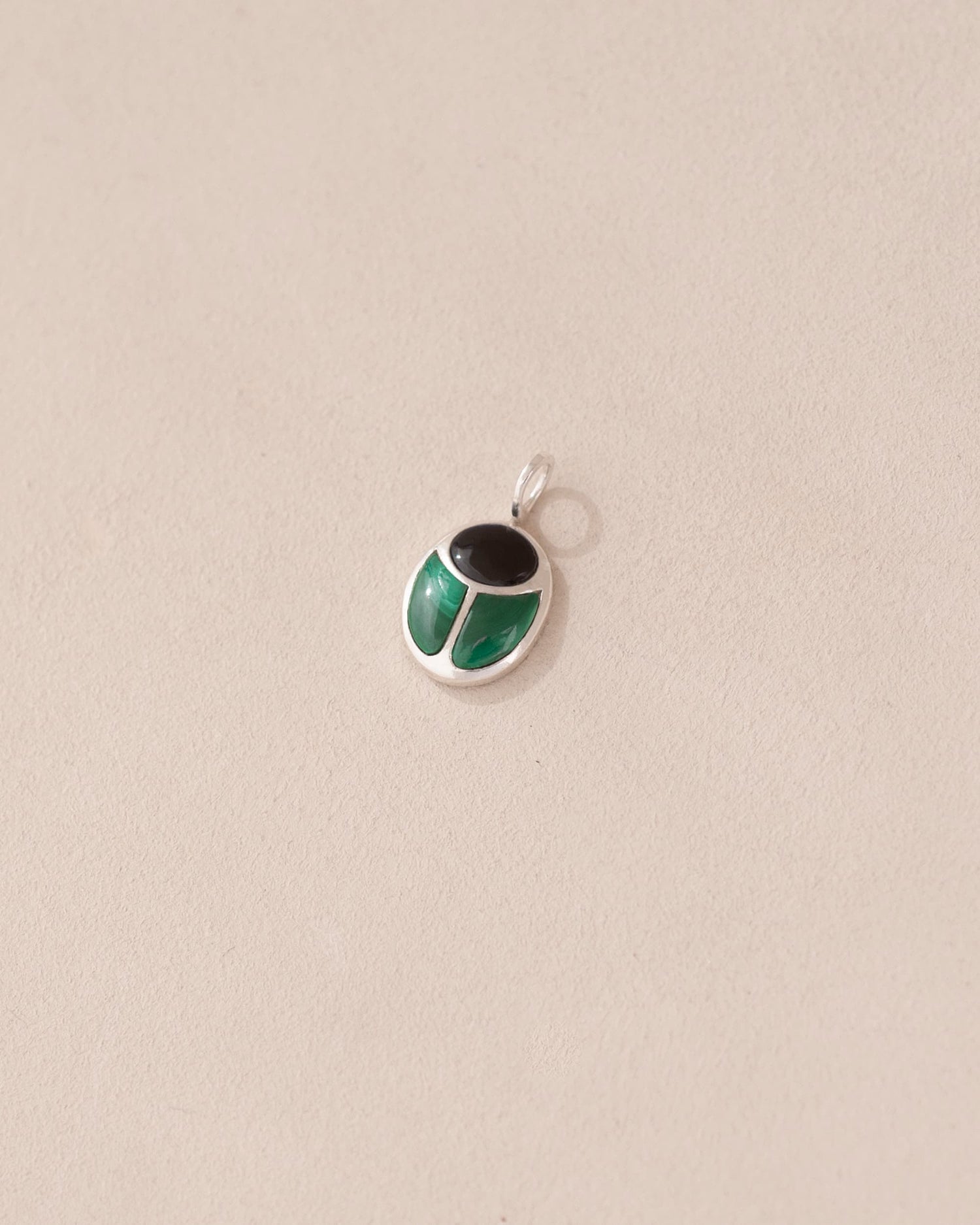 A silver charm with onyx and malachite colors, designed in the shape of a scarab amulet.
