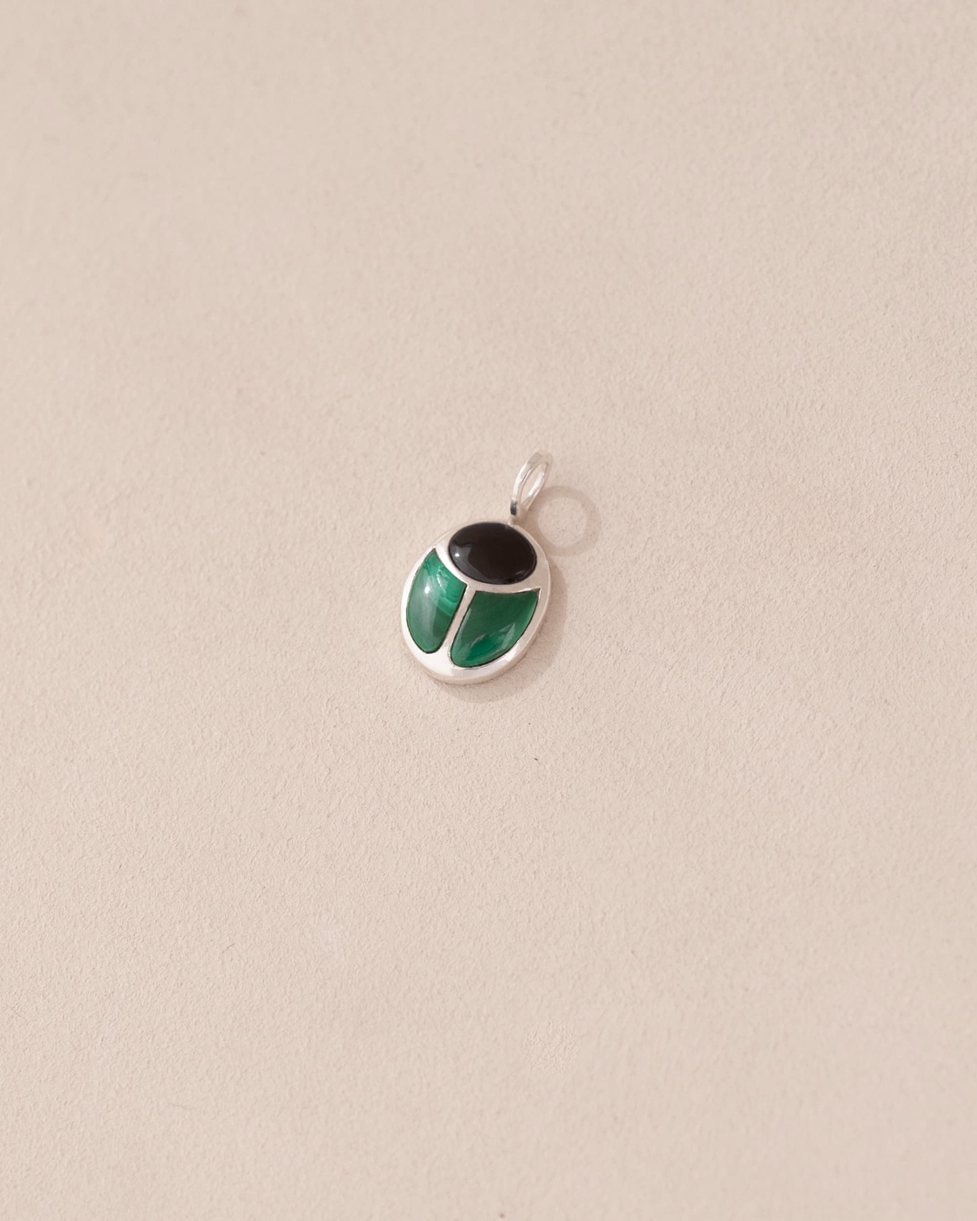 A silver charm with onyx and malachite colors, designed in the shape of a scarab amulet.