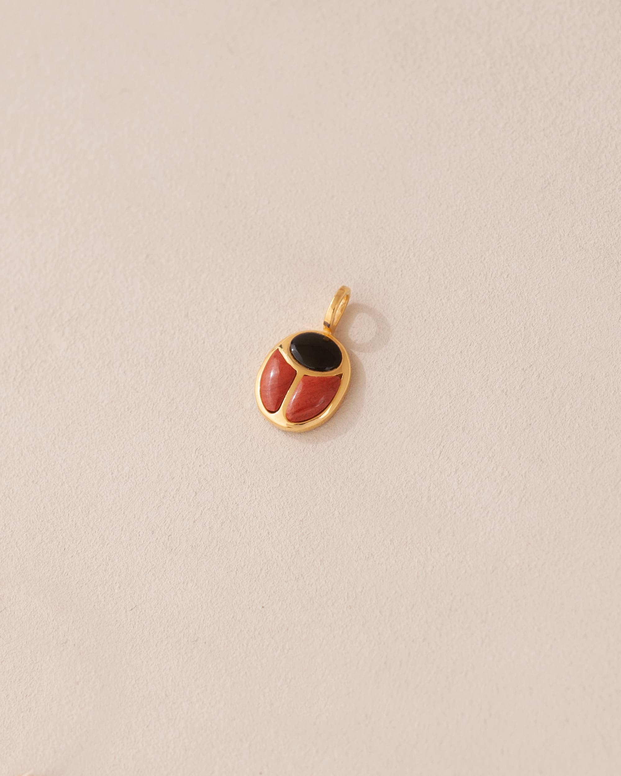 A gold charm featuring a scarab design with onyx and red jasper inlays, displayed against a neutral background.