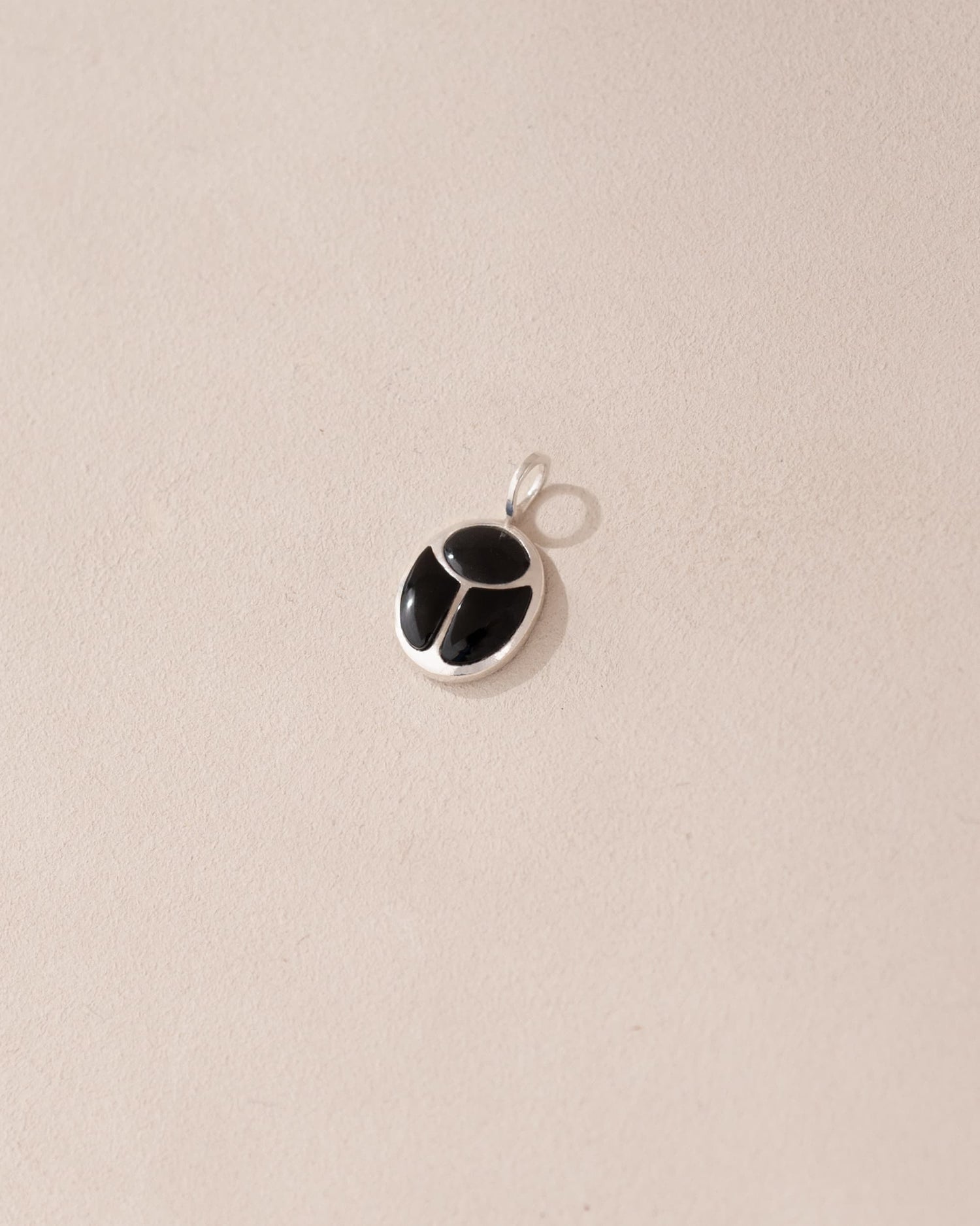 A silver-colored charm with an onyx-like black center, displayed against a beige background.