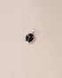 A silver-colored charm with an onyx-like black center, displayed against a beige background.